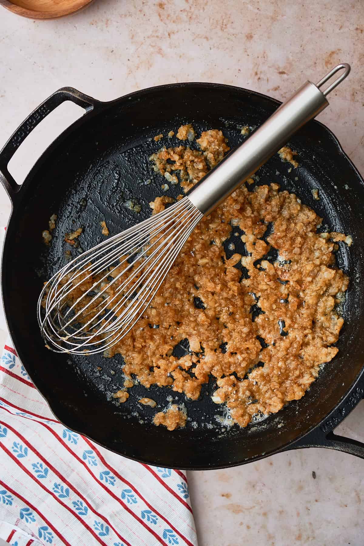 Deep golden brown flour in a skillet with onions and a whisk.