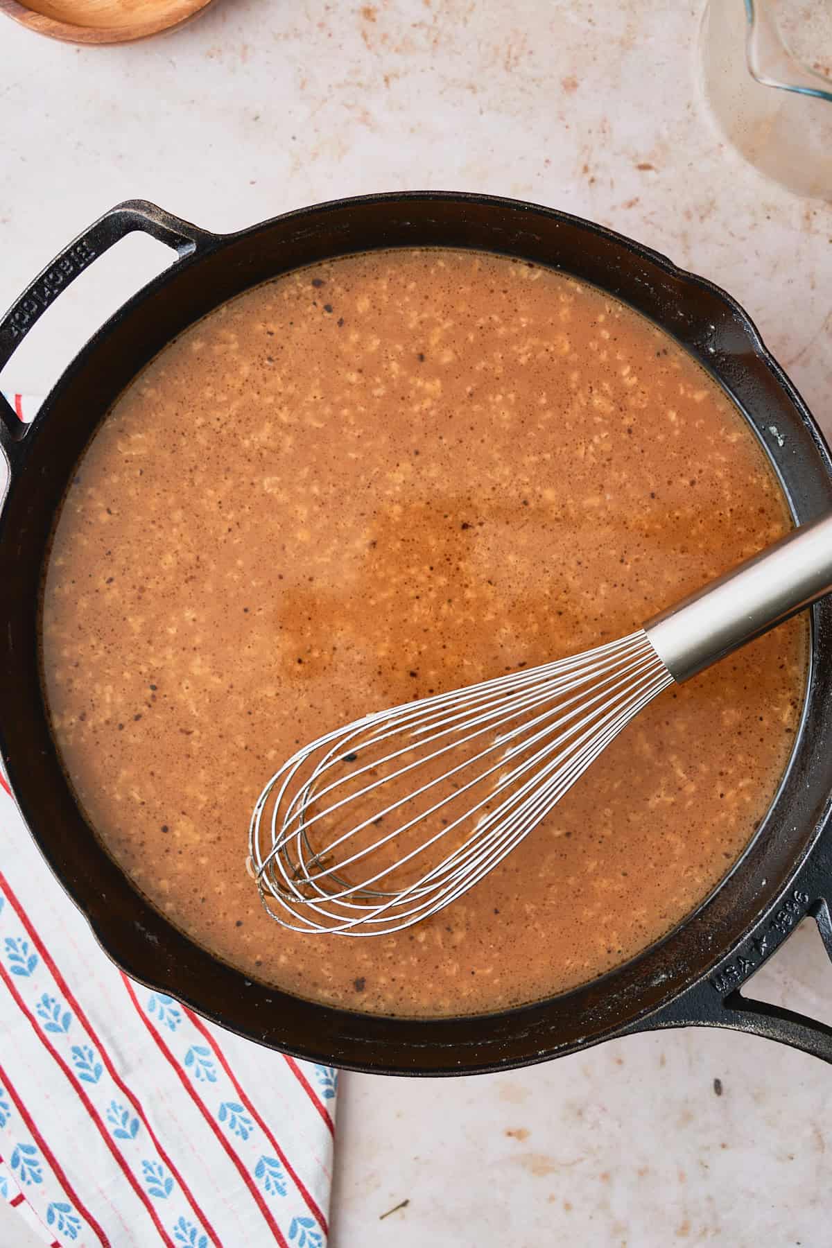 Beef broth added to a skillet and being whisked in to make a brown gravy.