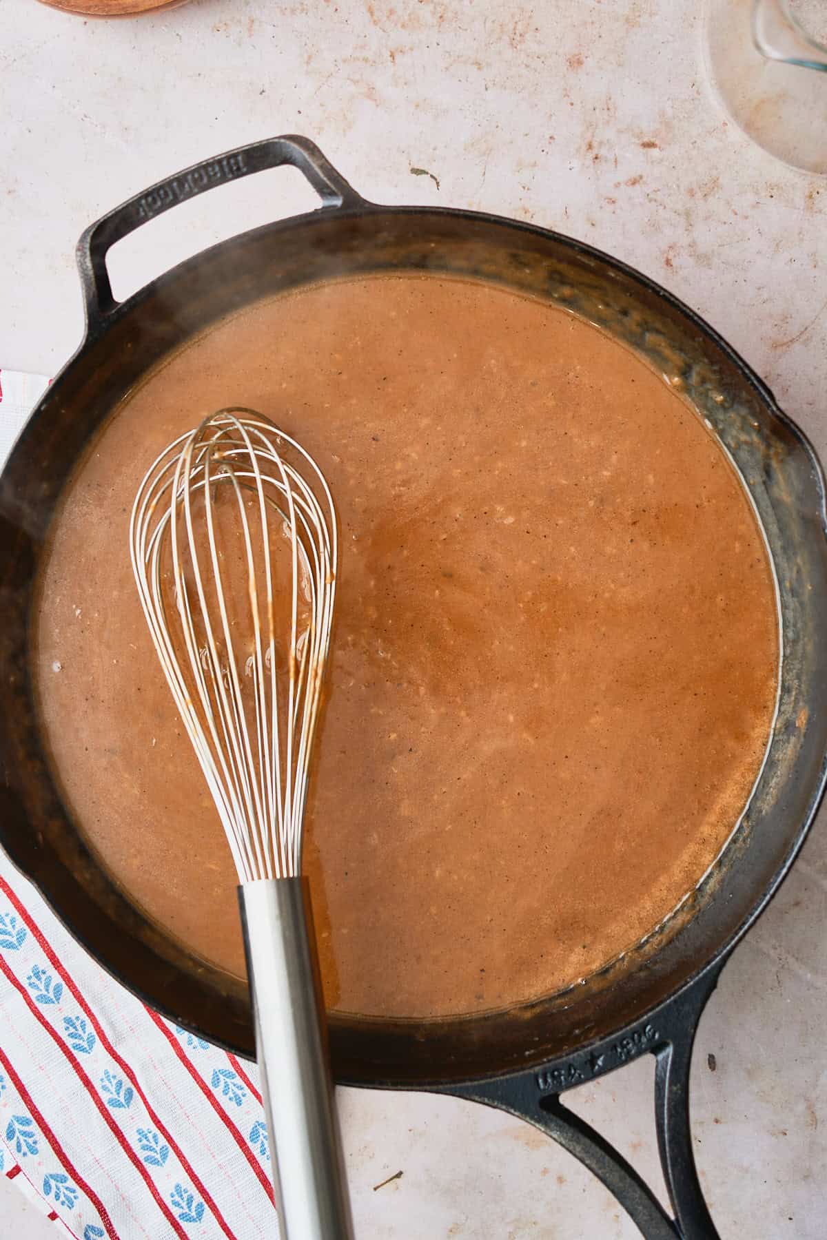 Thickened brown gravy for meatballs in a skillet with a whisk.