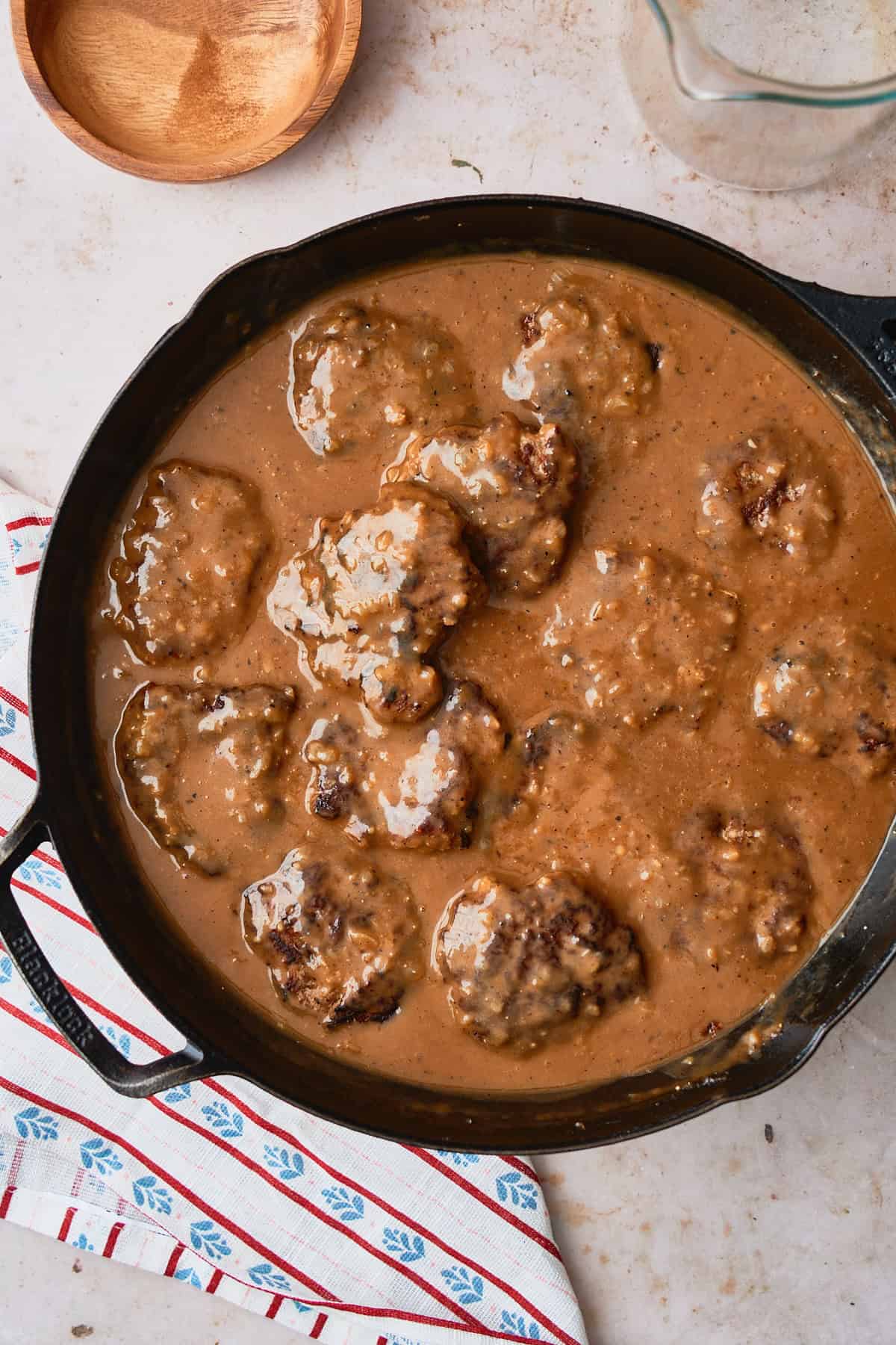 Norwegian style meatball patties in a large cast iron skillet covered in brown gravy.