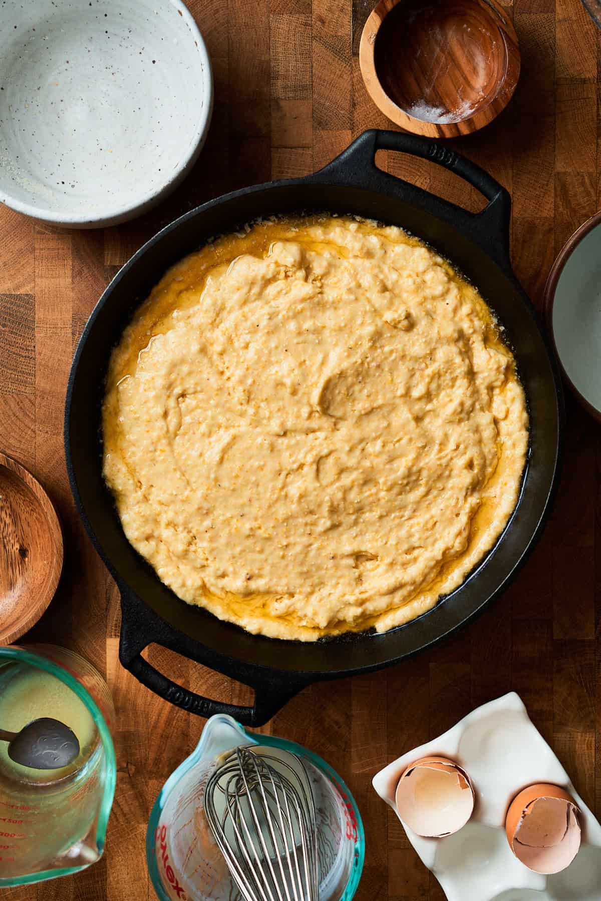 Raw cornbread batter in a cast iron skillet with melted butter pooling in the pan.