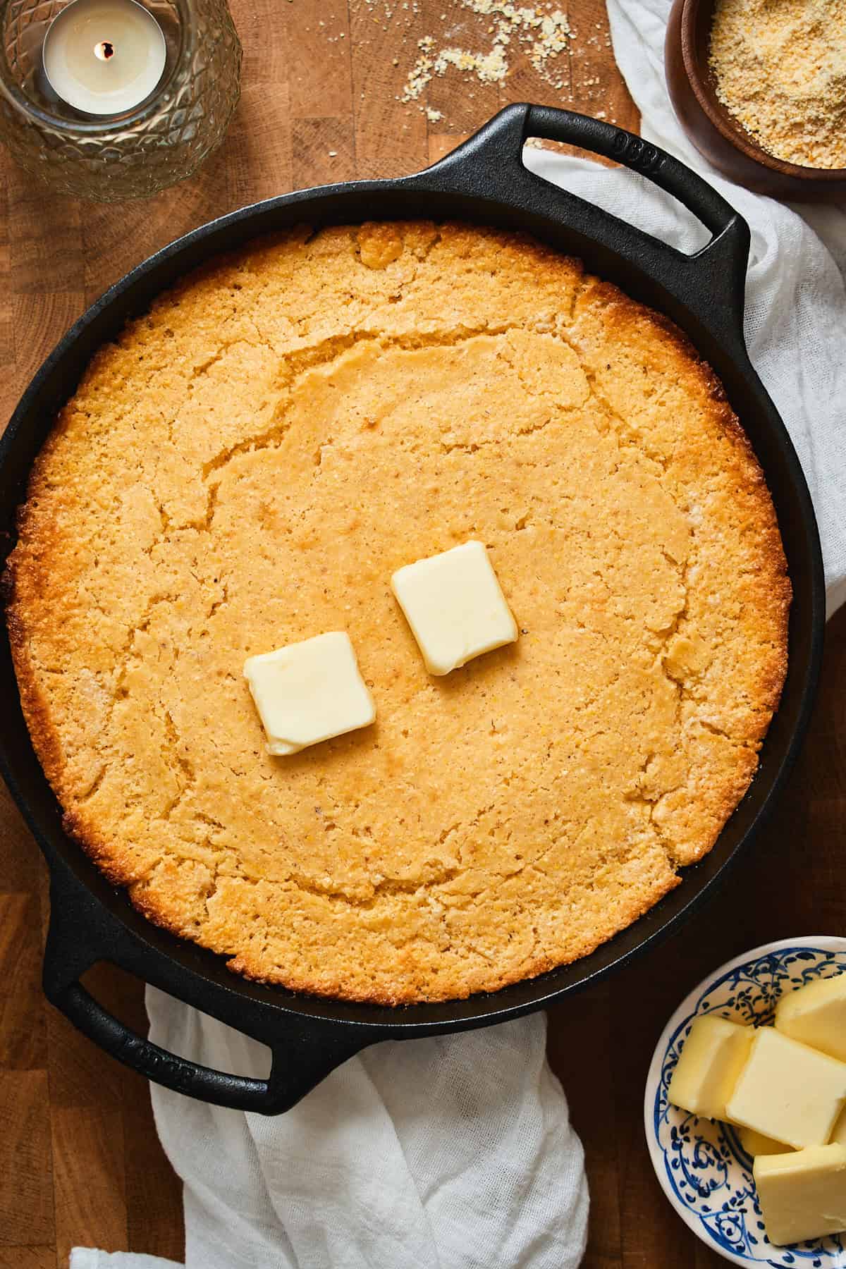 Baked cornbread in a cast iron skillet topped with two knobs of butter.