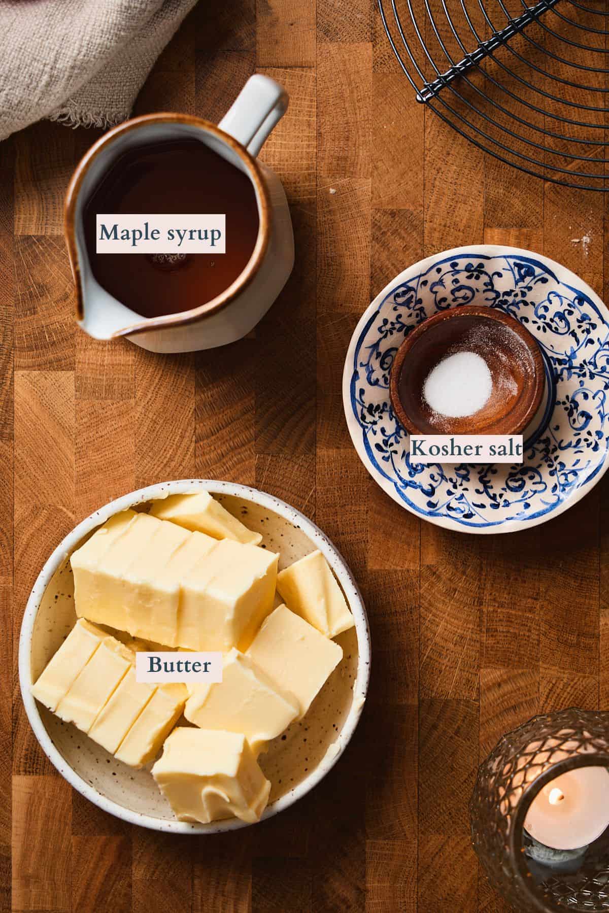 Ingredients to make whipped maple butter - softened butter, maple syrup, and kosher salt - labeled on a wooden table.
