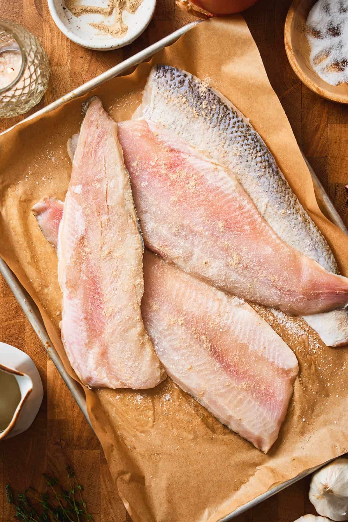 Seasoned fresh whitefish fillets on a parchment-lined sheet pan.