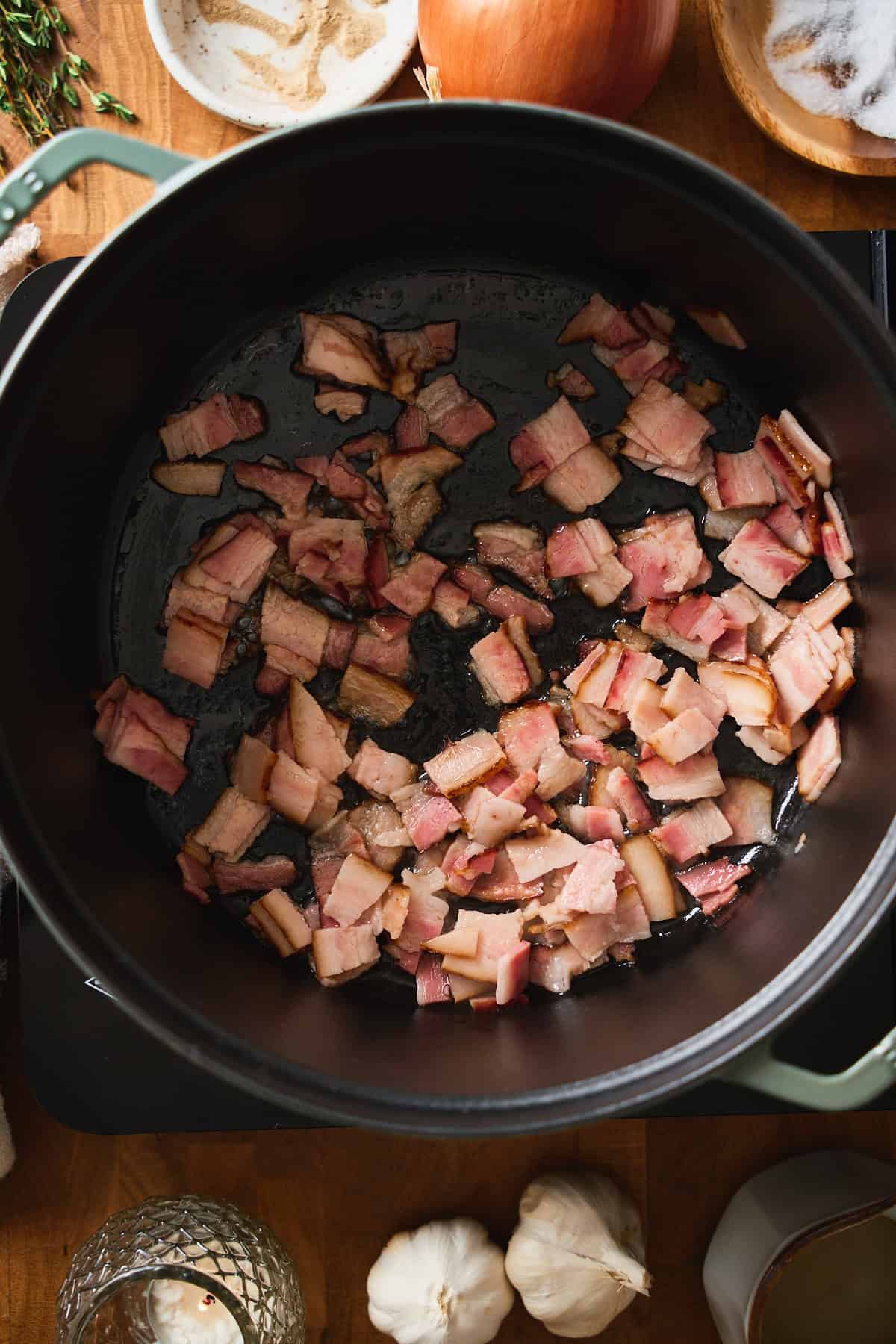Raw bacon pieces in a green Staub Dutch oven.