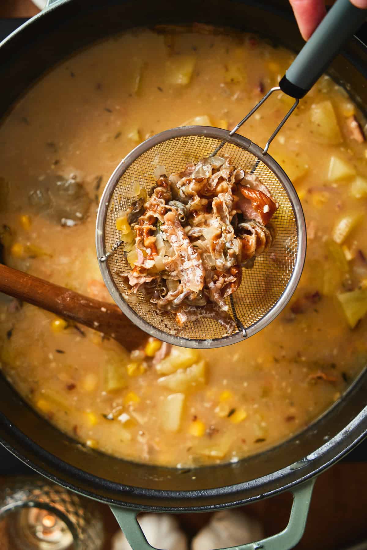 Smoked whitefish skin and aromatics being lifted out of the chowder with a strainer.