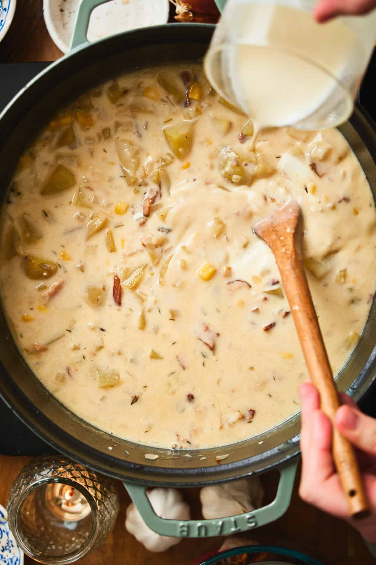 Heavy cream being poured into the chowder base while stirring with a wooden spoon.