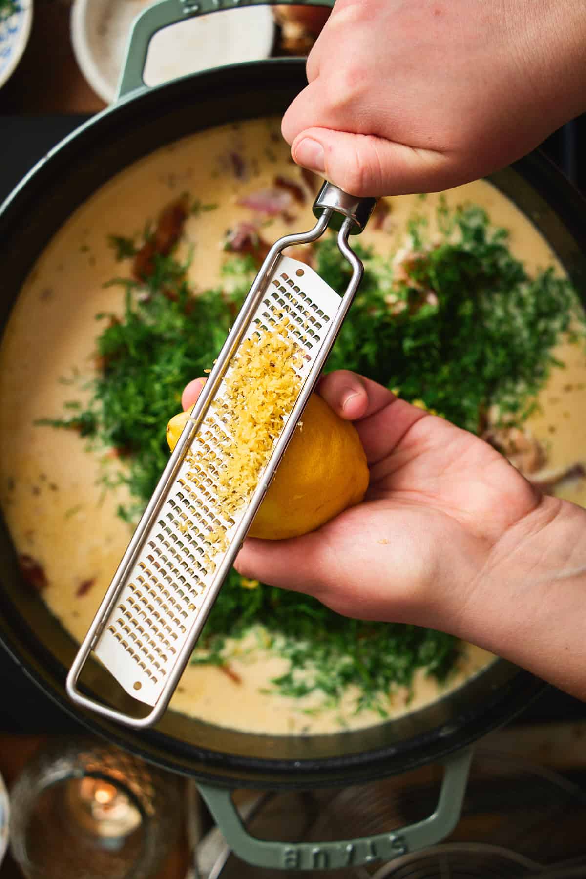 Lemon being zested with a microplane over the finished chowder with fresh dill.