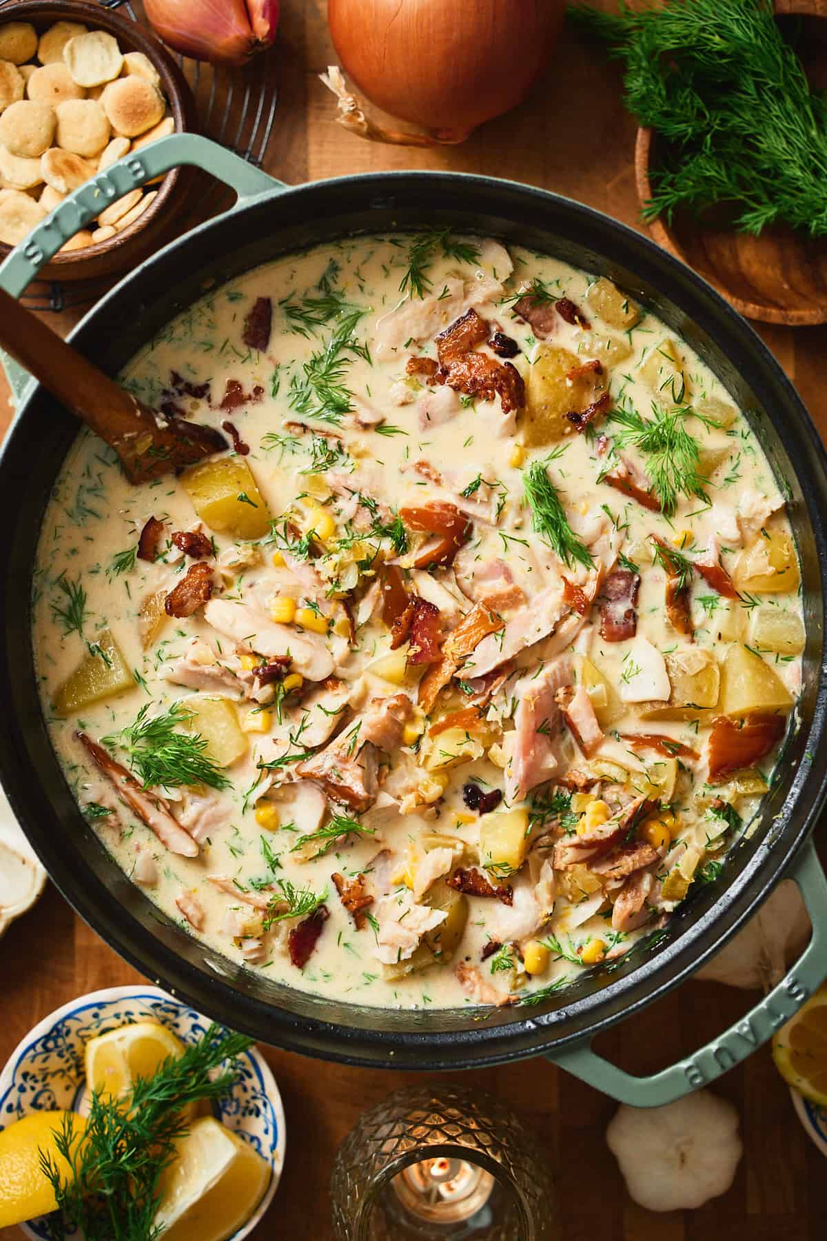 Overhead view of finished whitefish chowder in a green Staub Dutch oven with wooden spoon.