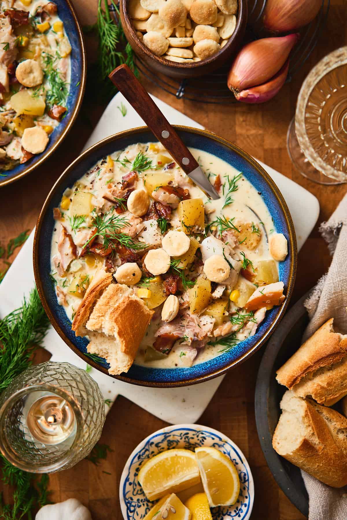 Overhead styled bowl of whitefish chowder with bread, oyster crackers, lemon, and wine.