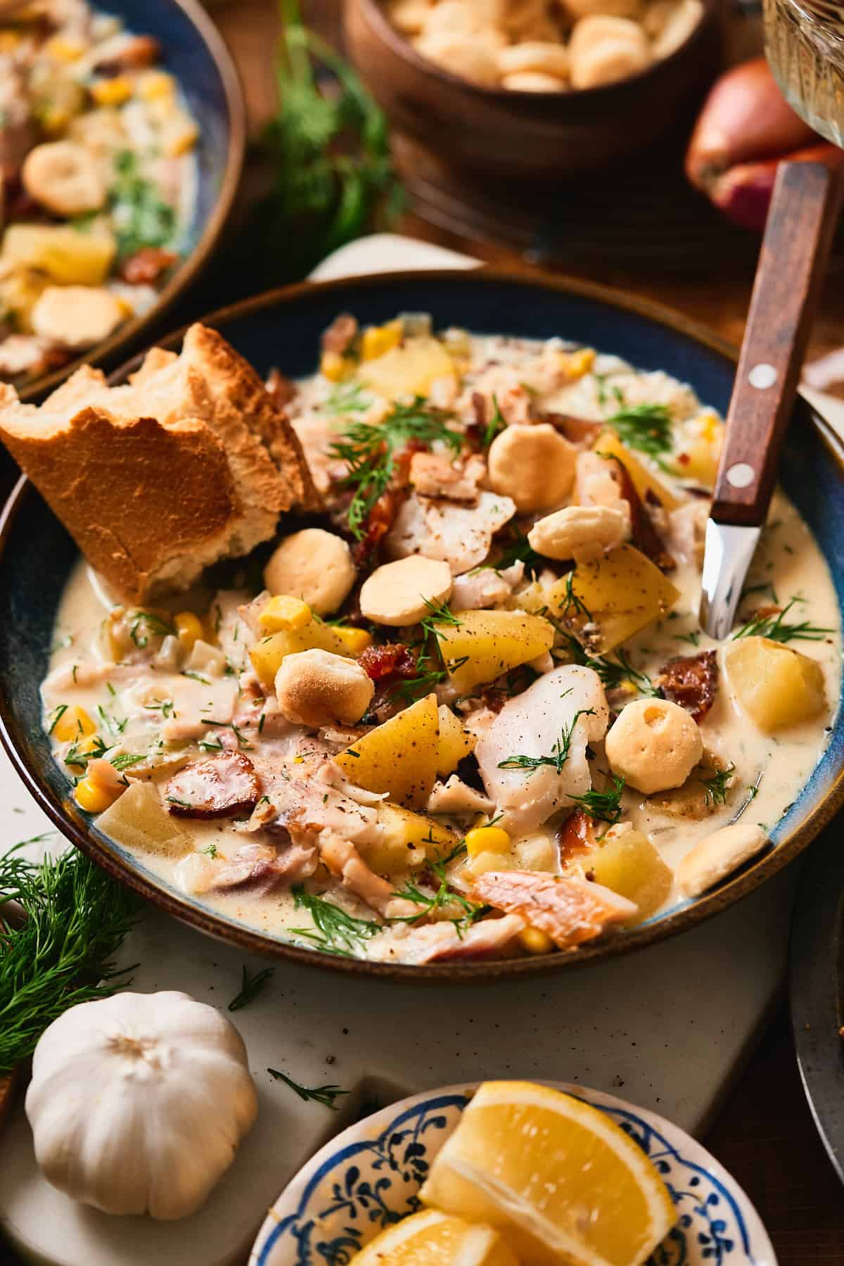 Creamy whitefish chowder with bacon, potatoes, corn, dill, and oyster crackers in a blue bowl with crusty bread.
