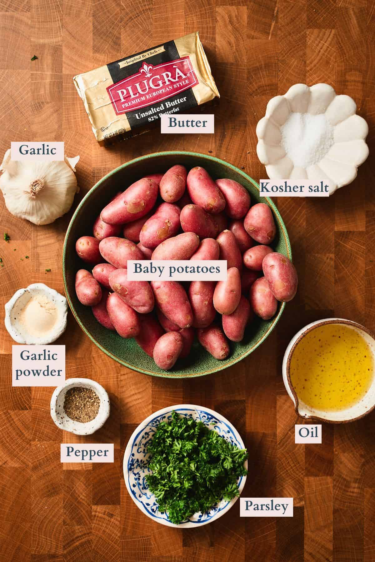 Ingredients for garlic butter roasted potatoes laid out and labeled on a wooden surface.