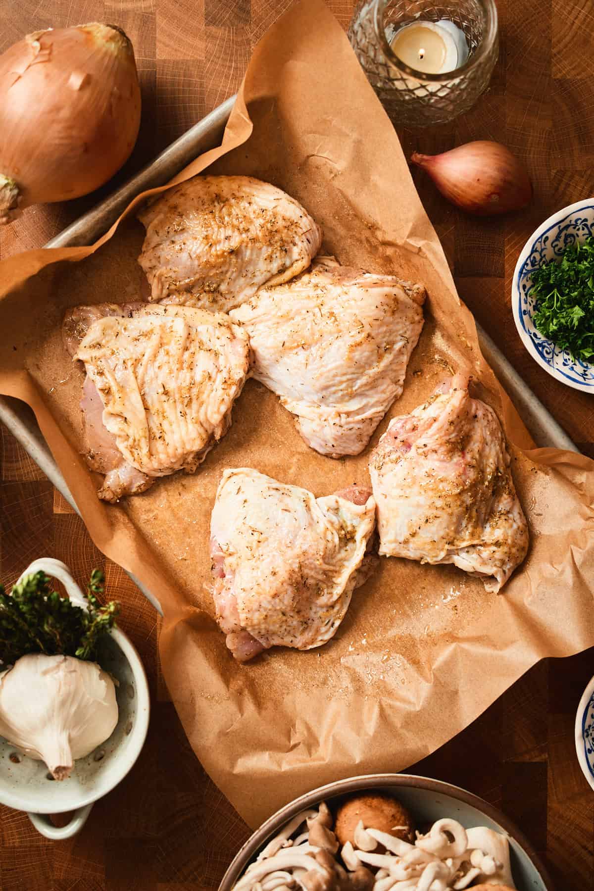 Chicken thighs with skin on seasoned well on a baking sheet.