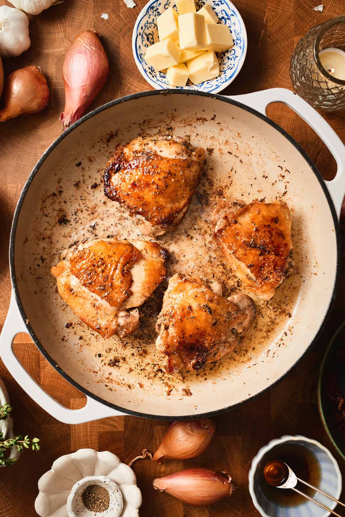 Golden brown chicken thighs with the skin on in a white skillet.