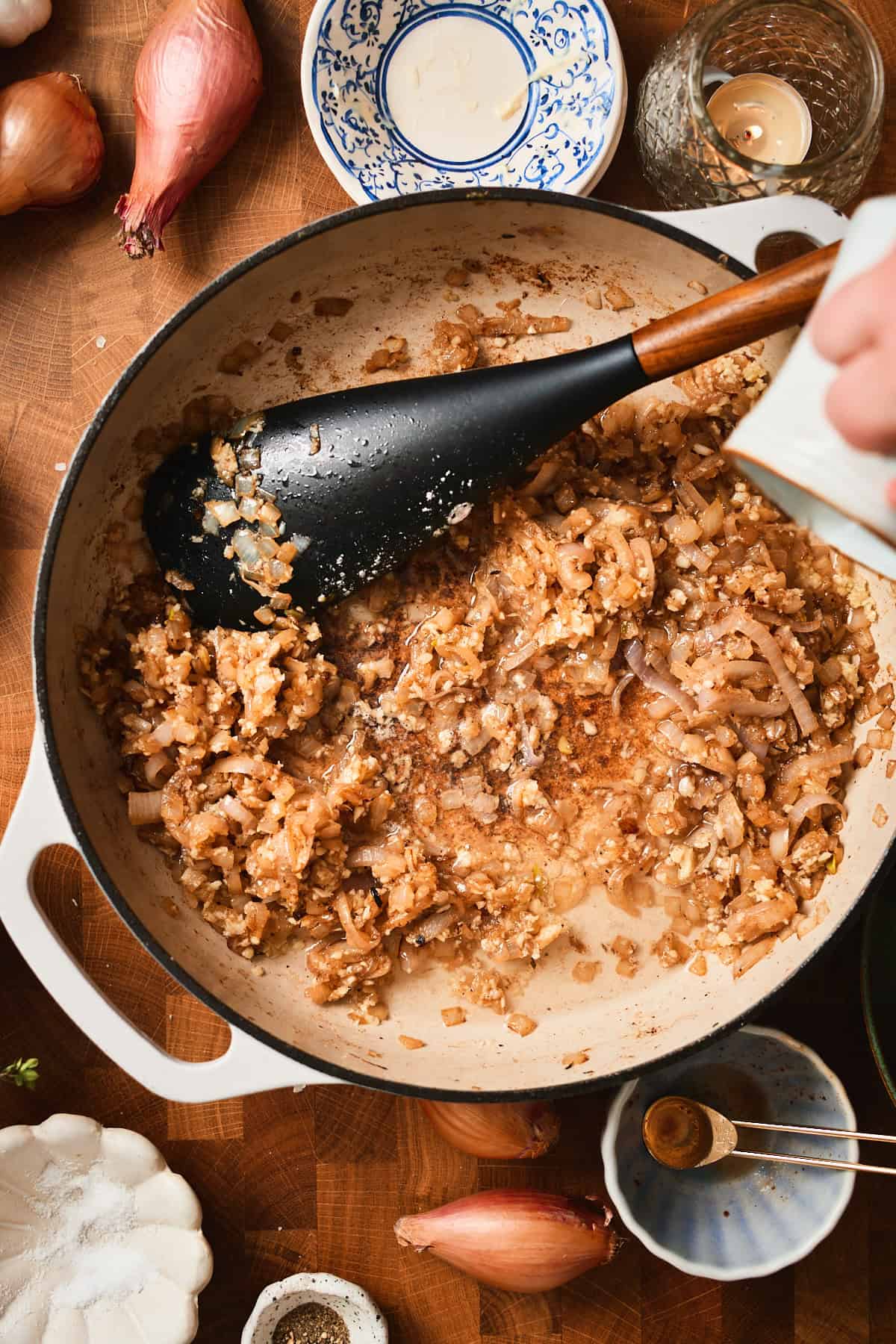Hand pouring in white wine to a skillet with onions and shallots to deglaze.
