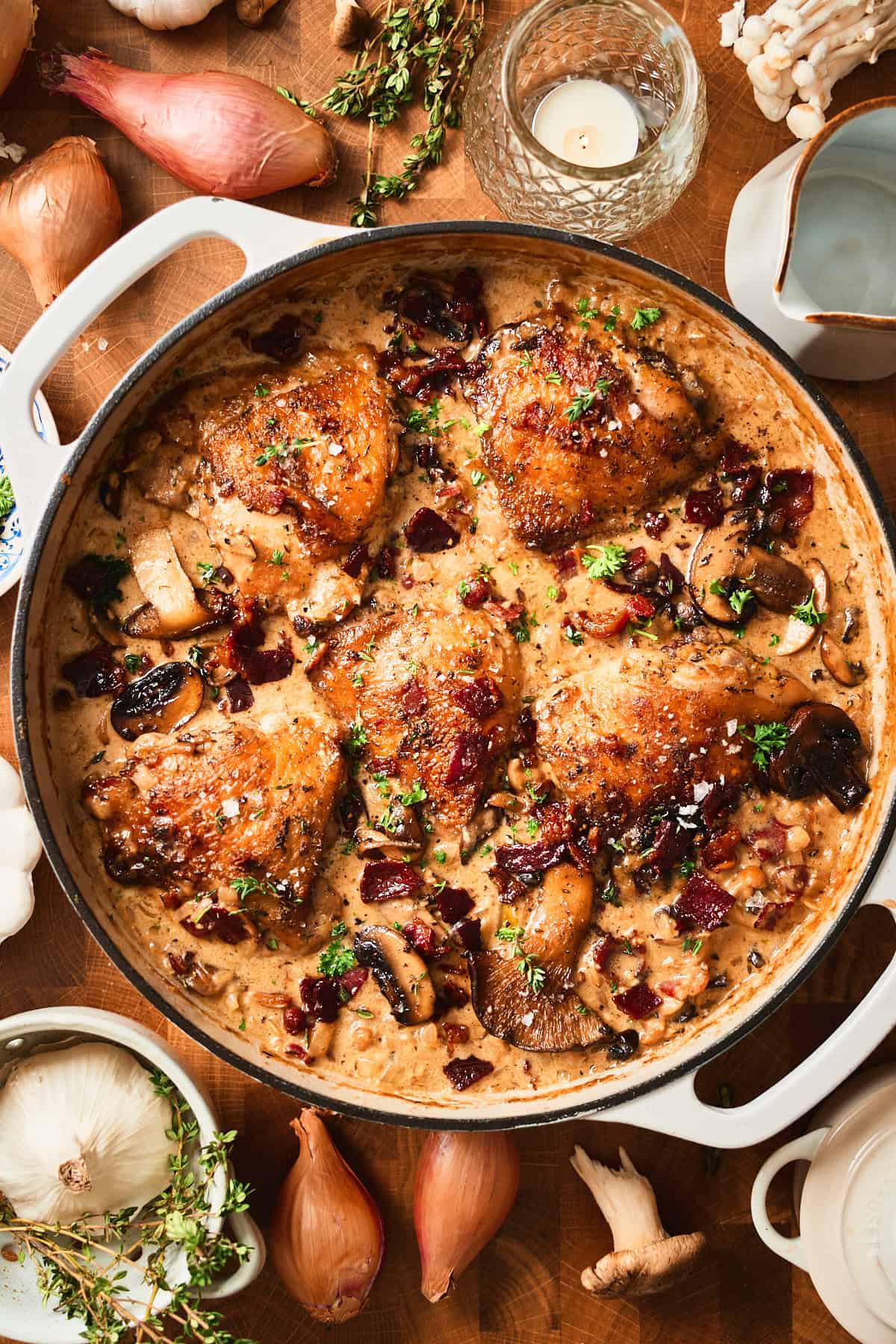 Creamy mushroom chicken thighs with beef bacon in a white skillet, overhead view.