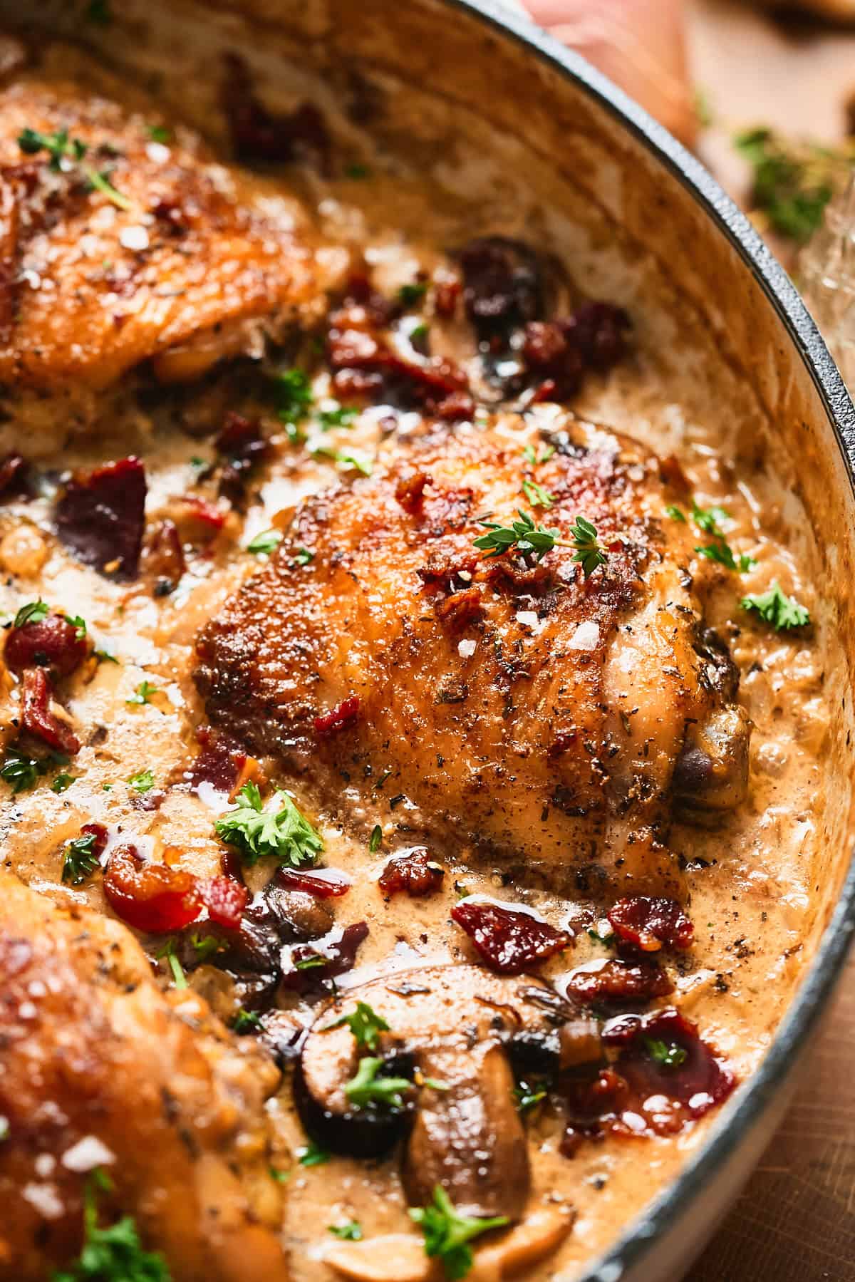 Close-up of a creamy mushroom chicken thigh with crispy beef bacon and fresh herbs in cream sauce.