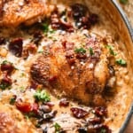 Close-up of a creamy mushroom chicken thigh with crispy beef bacon and fresh herbs in a rich cream sauce in a skillet.
