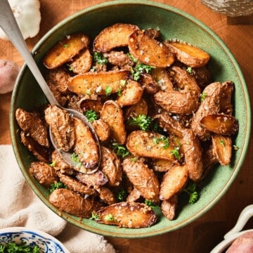Golden brown garlic butter roasted baby potatoes in a green bowl surrounded by fresh ingredients.