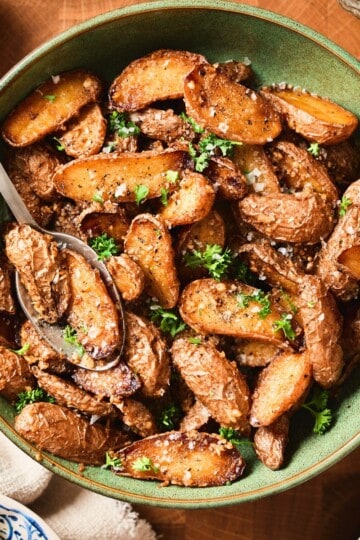 Golden brown garlic butter roasted baby potatoes in a green bowl surrounded by fresh ingredients.