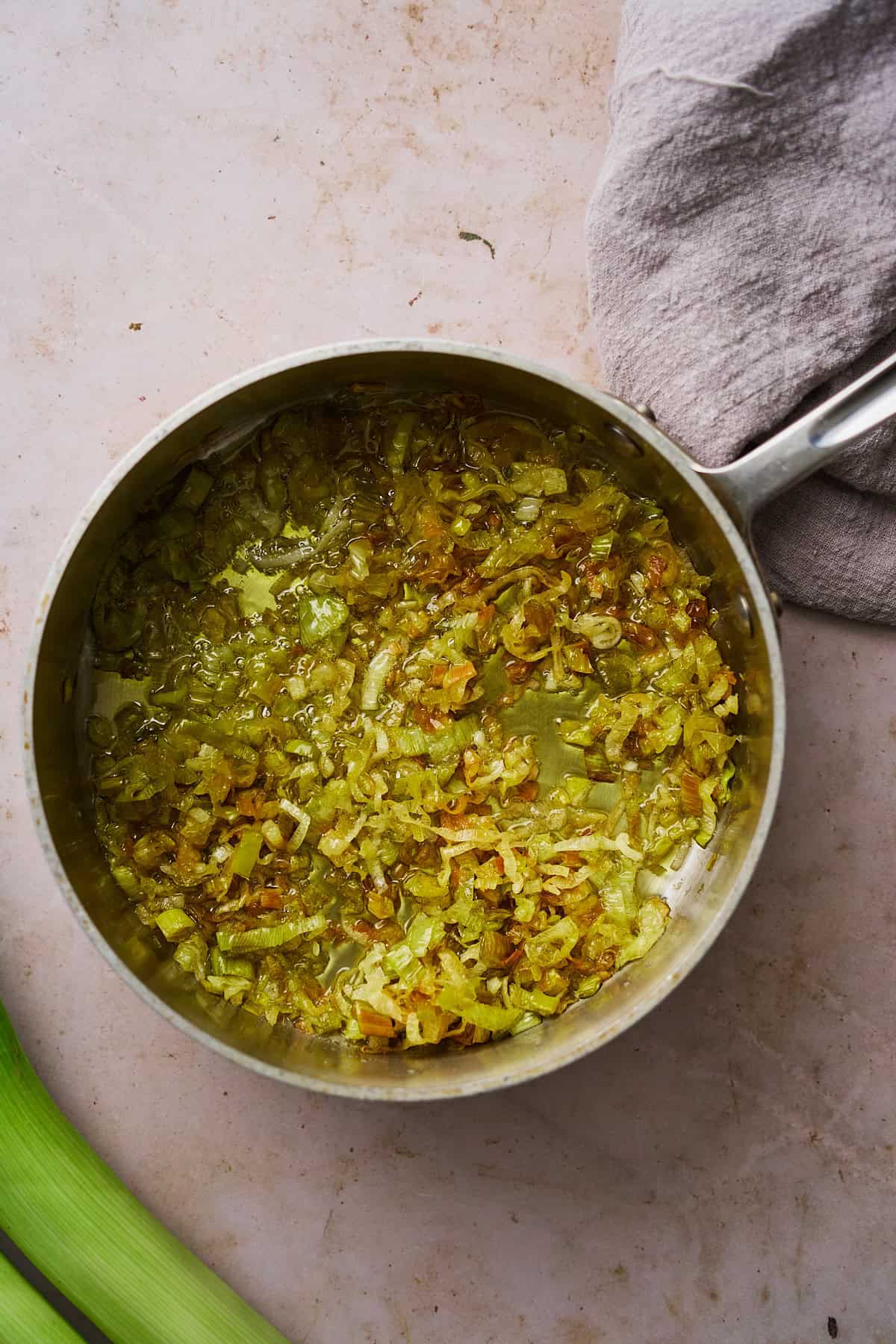 Light green leeks beginning to turn golden brown in oil in a saucepan.