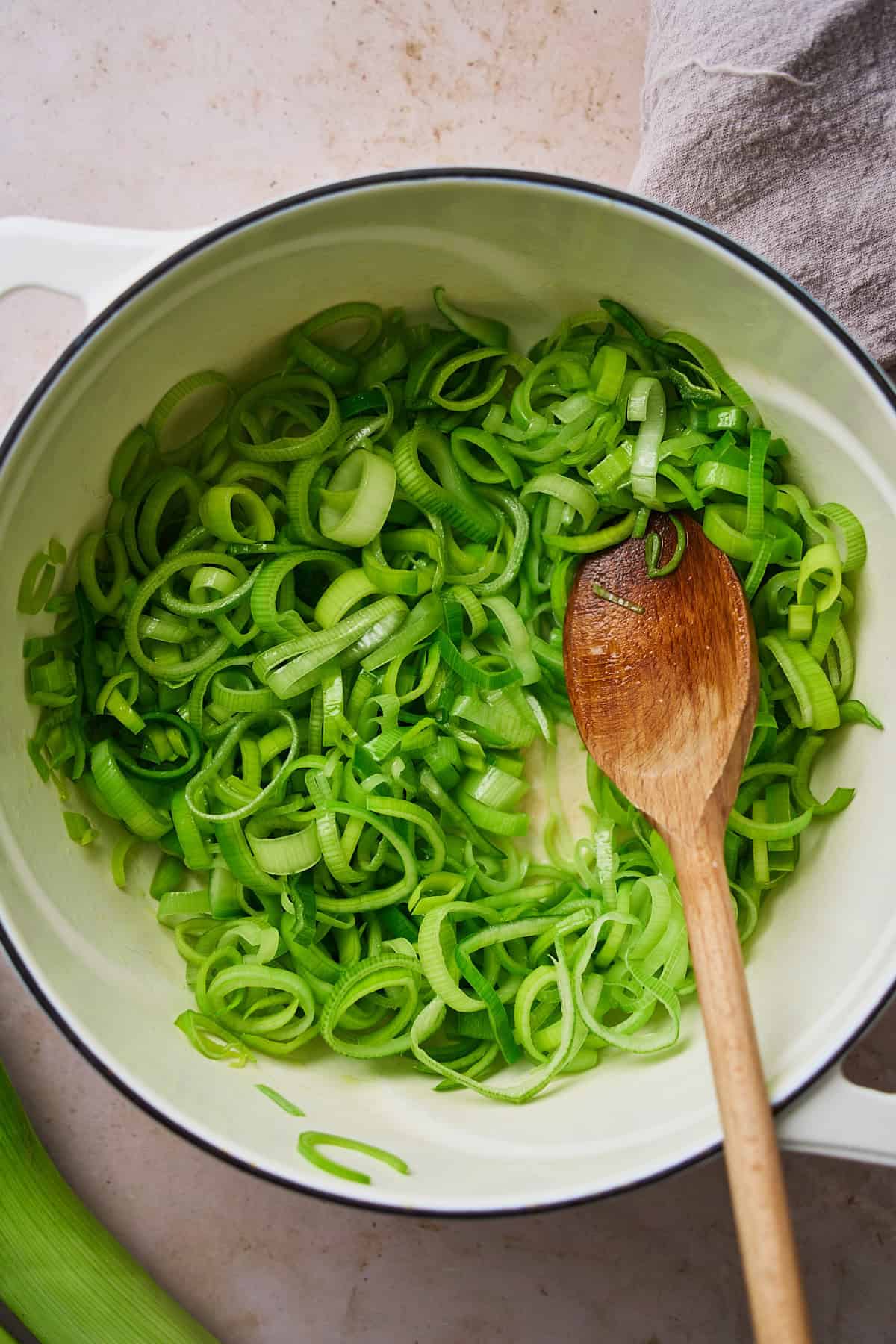 Dark green parts of leeks in a large dutch oven with a wooden spoon.