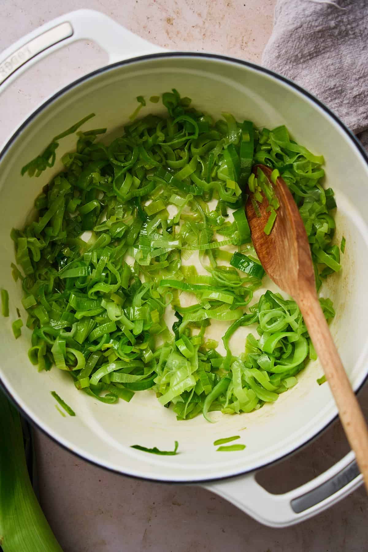 Dark green parts of leeks cooking down in a dutch oven.
