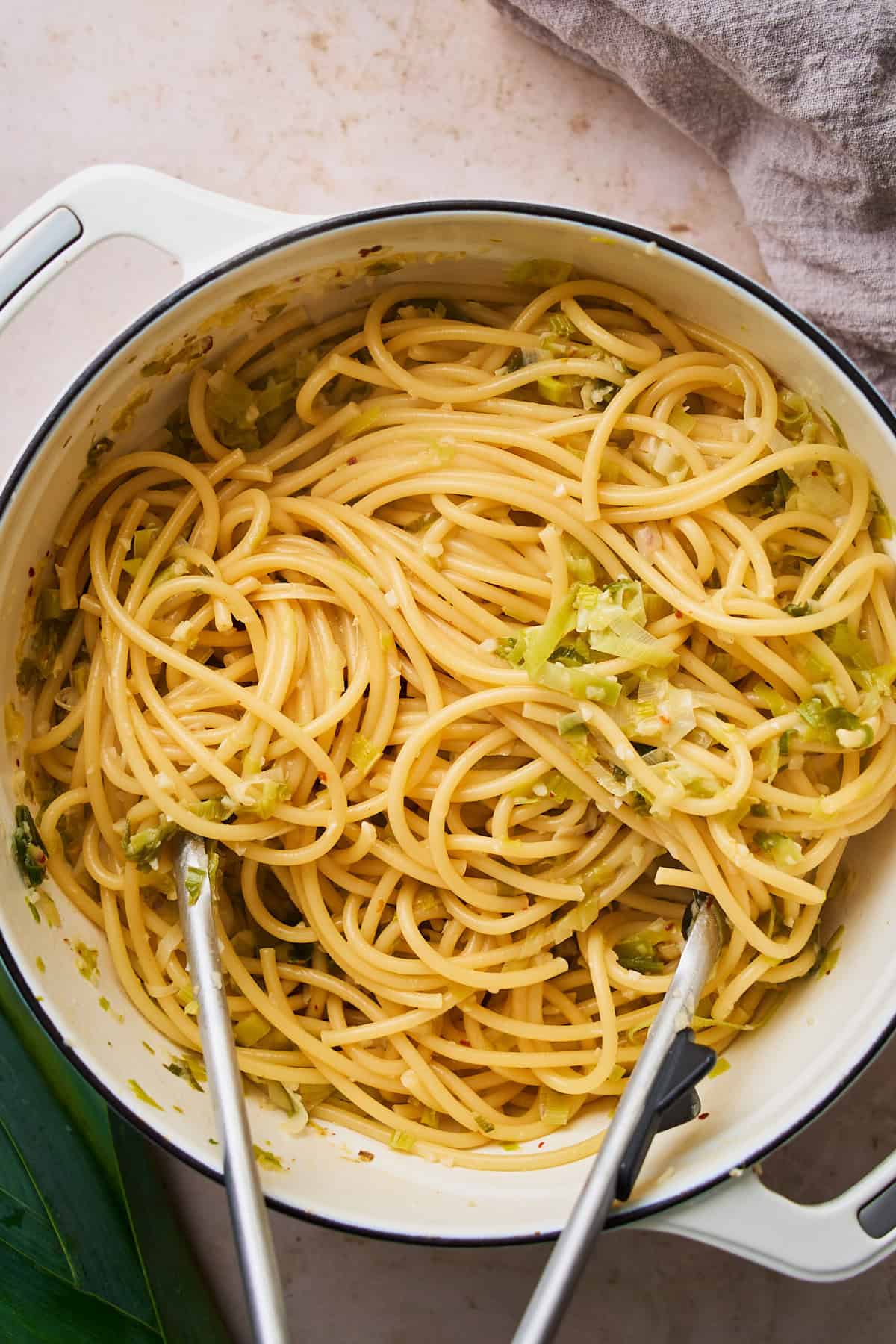 Cooked bucatini pasta added to a dutch oven with cooked leeks.