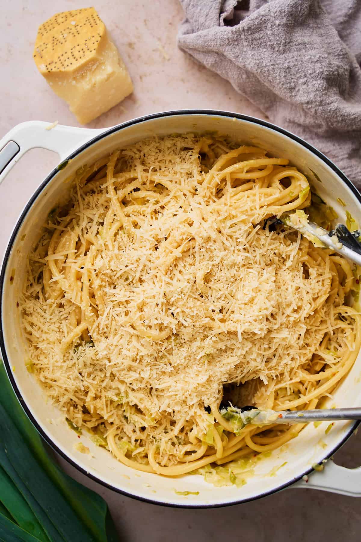 Cooked bucatini pasta added to a dutch oven and topped with parmesan cheese.
