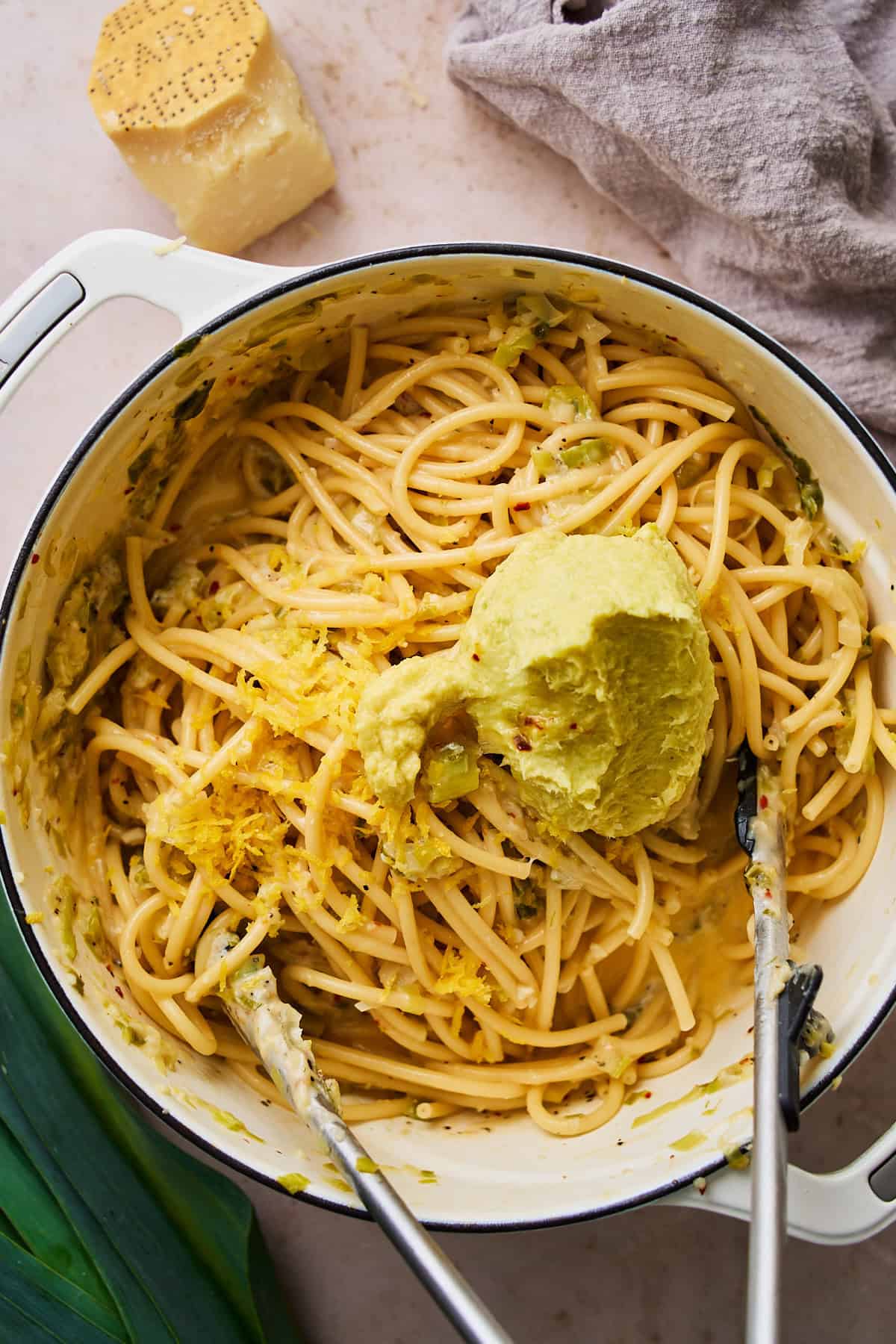 Large scoop of leek butter added to bucatini in a pot.