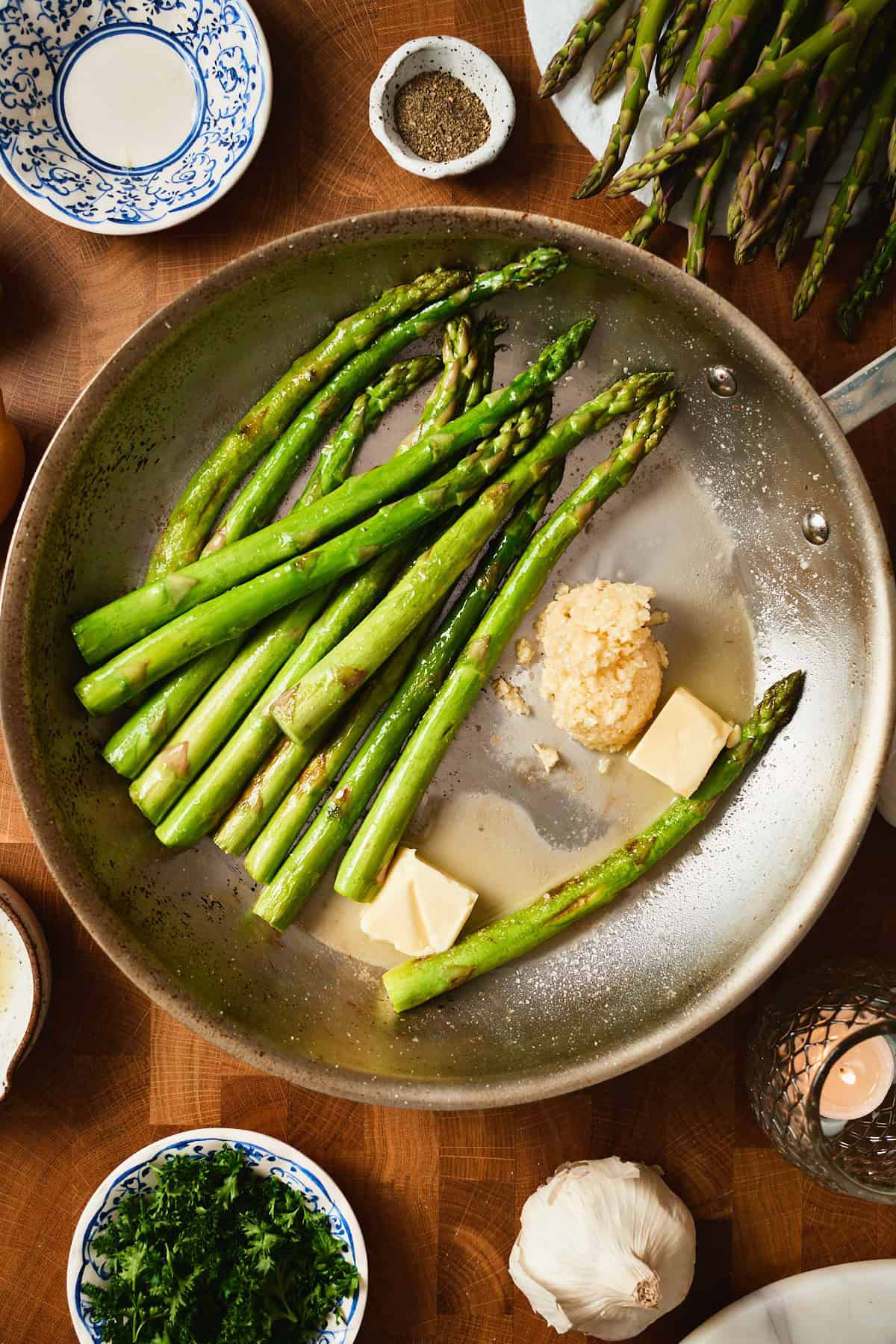 Cooked asparagus pushed to one side of the skillet with pats of butter melting alongside and lots of garlic.
