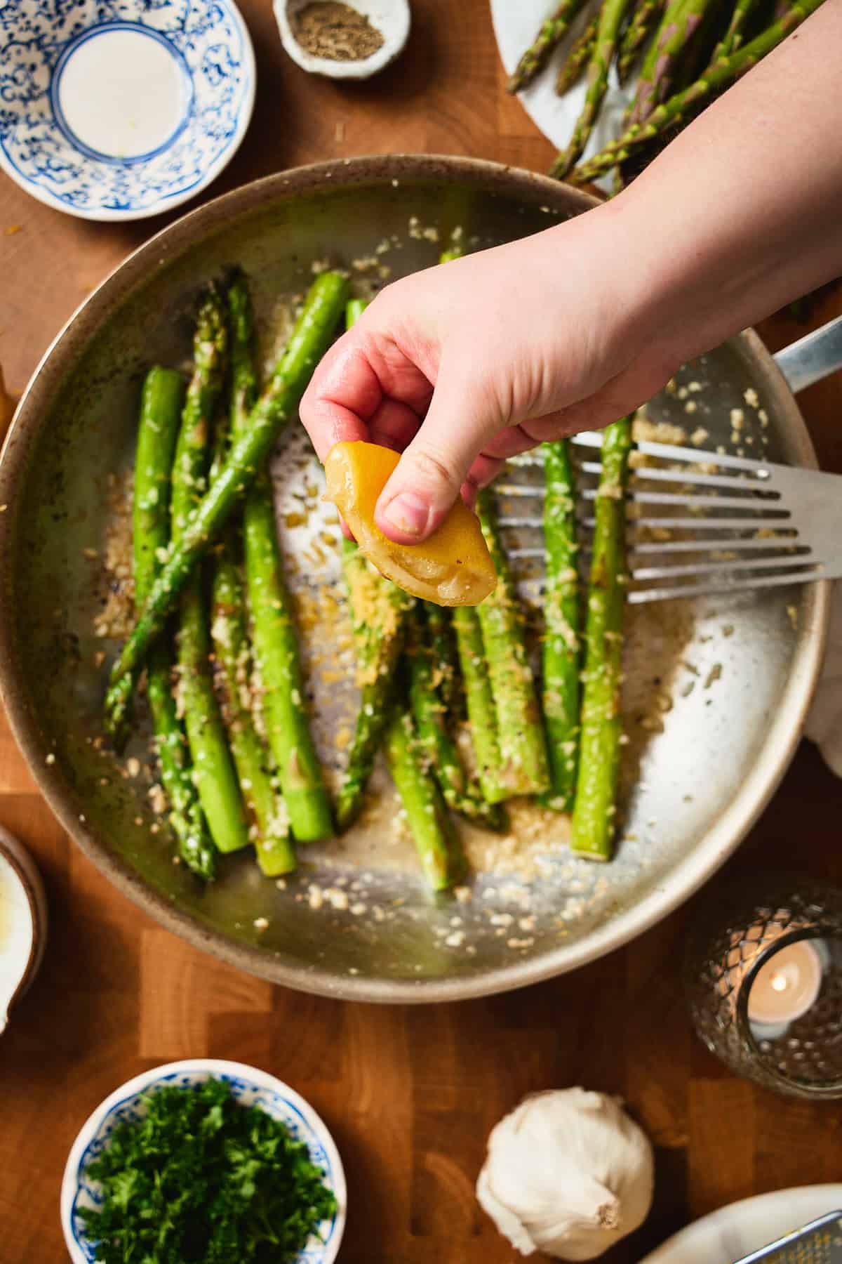 Hand squeezing fresh lemon juice over sautéed asparagus in a skillet.