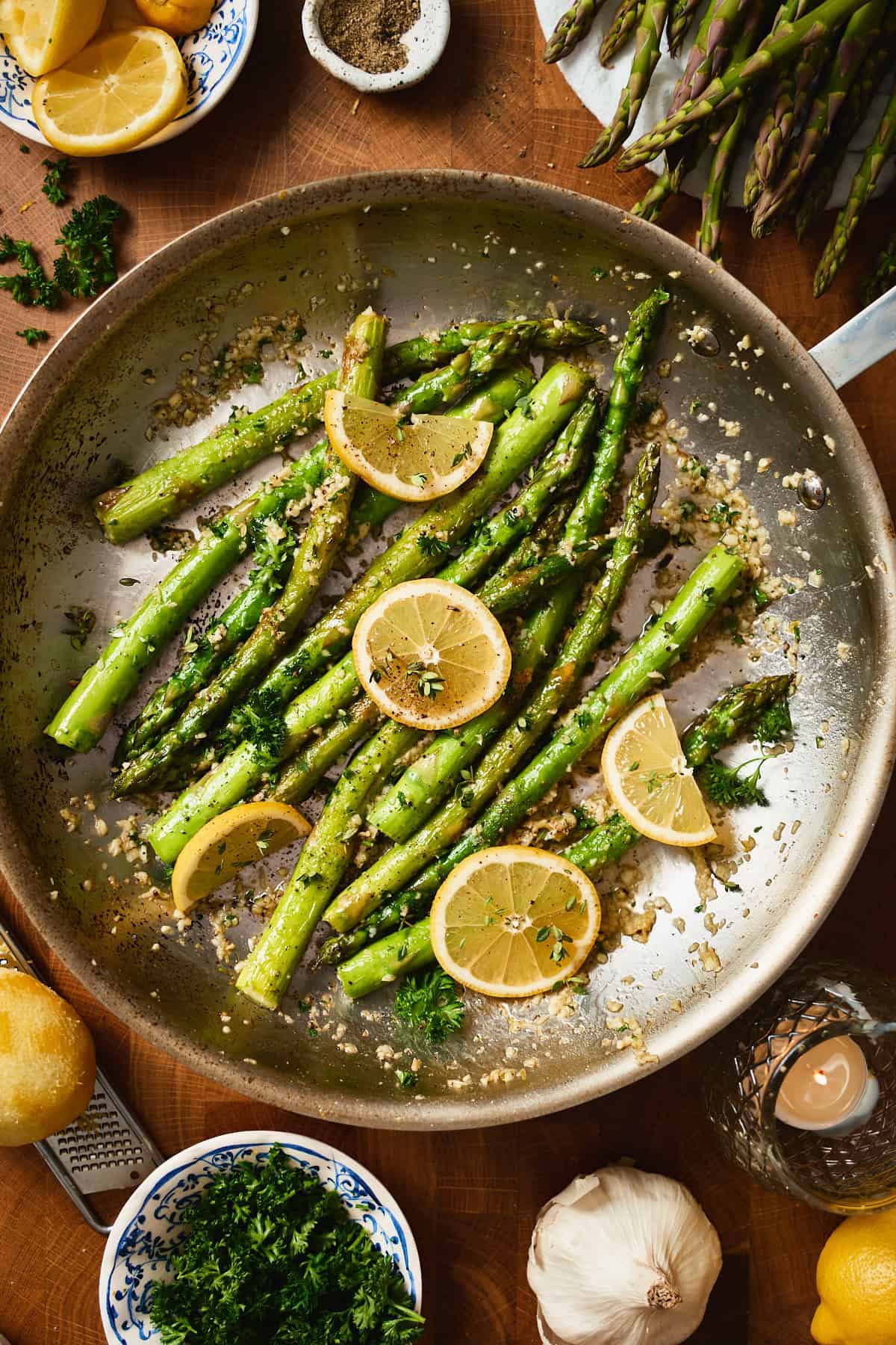 Overhead shot of pan fried asparagus with lemon garlic butter in a skillet, garnished with lemon slices, parsley, and herbs.
