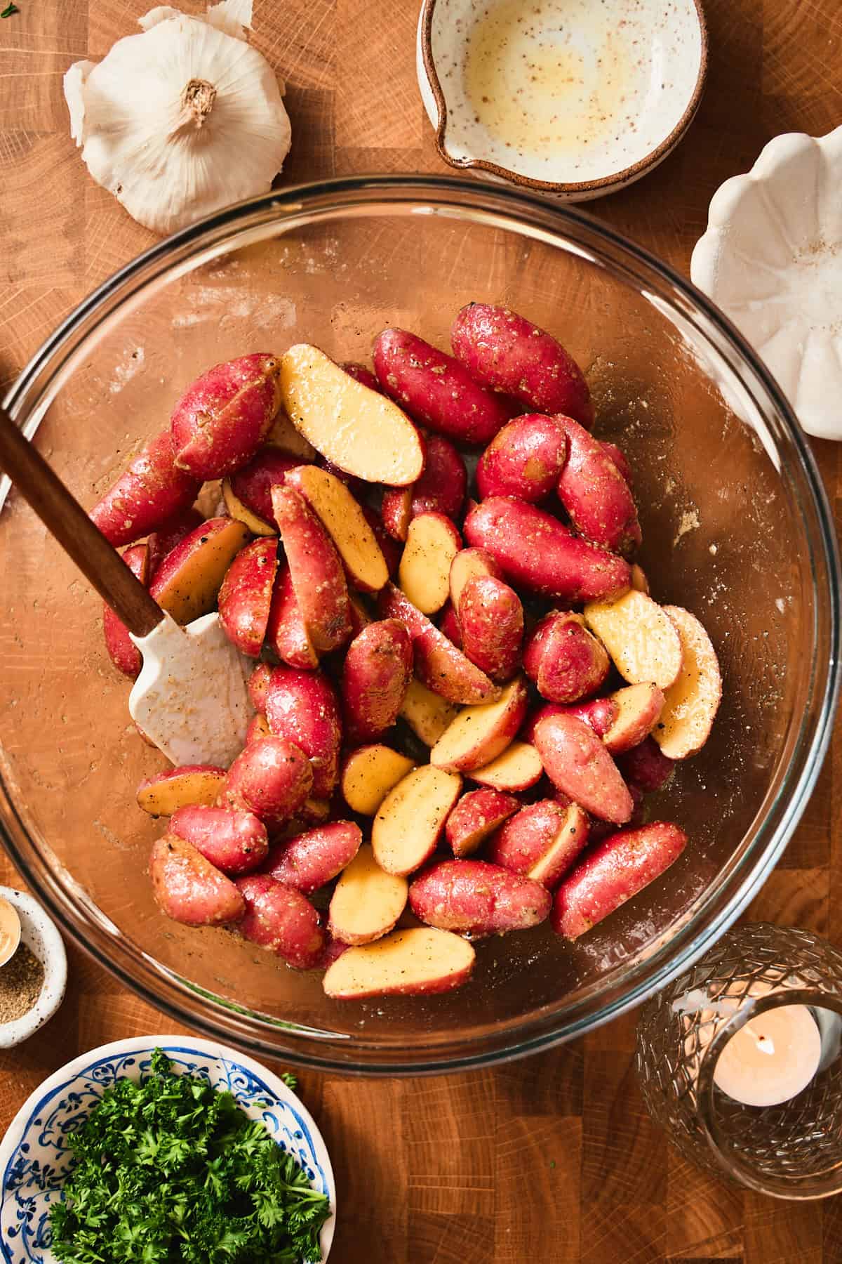 Halved baby potatoes in a bowl coated with oil and seasonings tossed together.