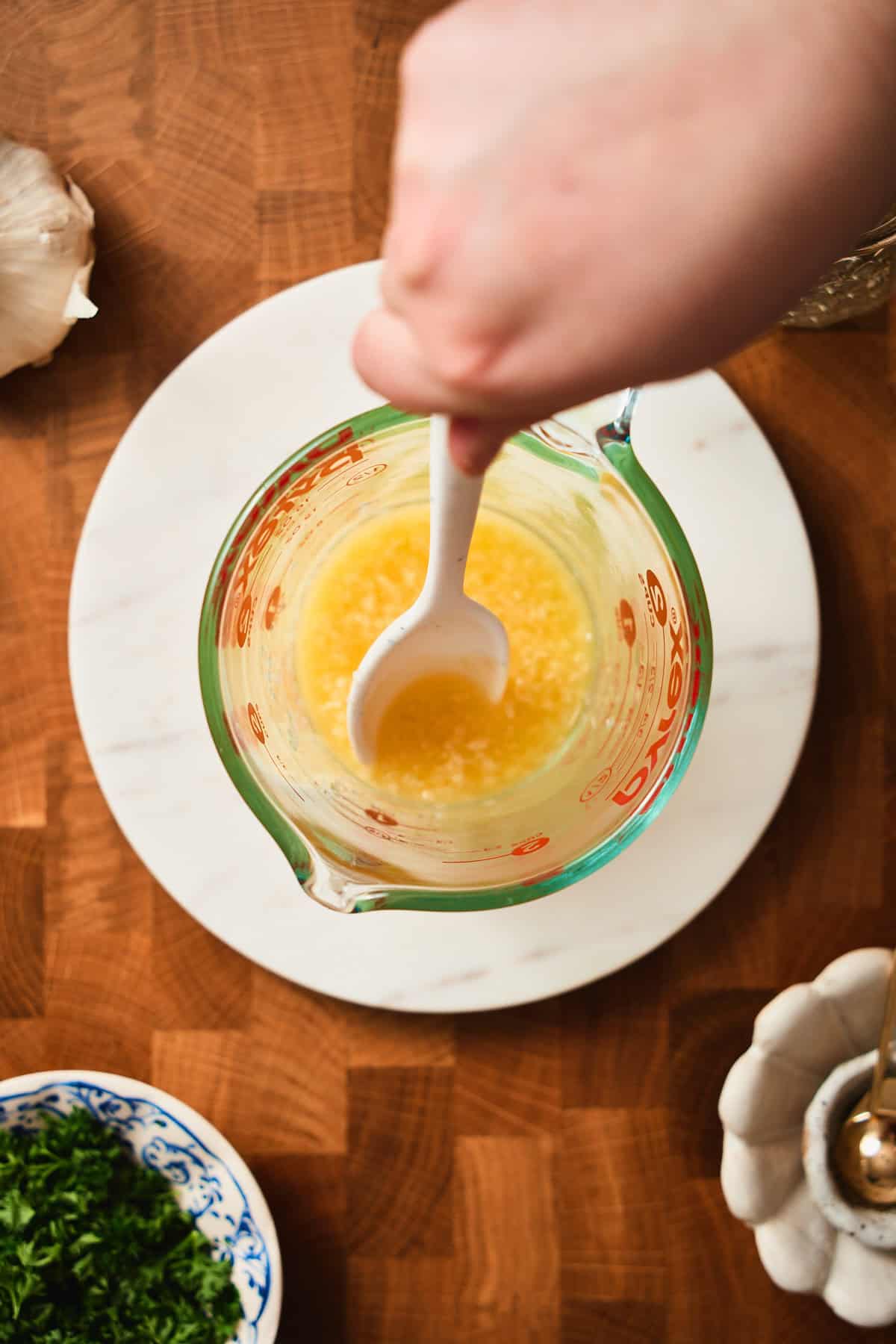 Hand mixing ip melted butter and minced garlic in a glass cup.