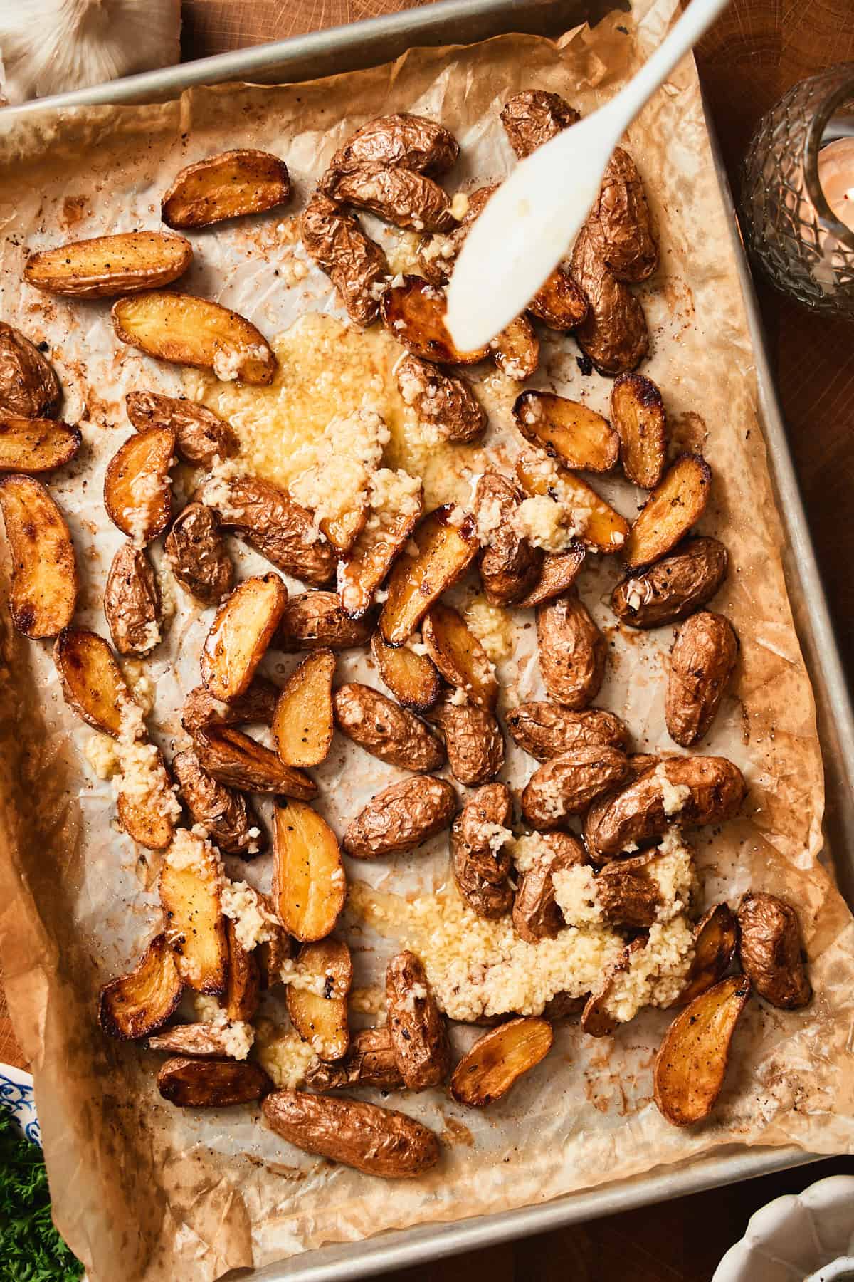 Adding garlic butter to a tray of roasted potatoes.