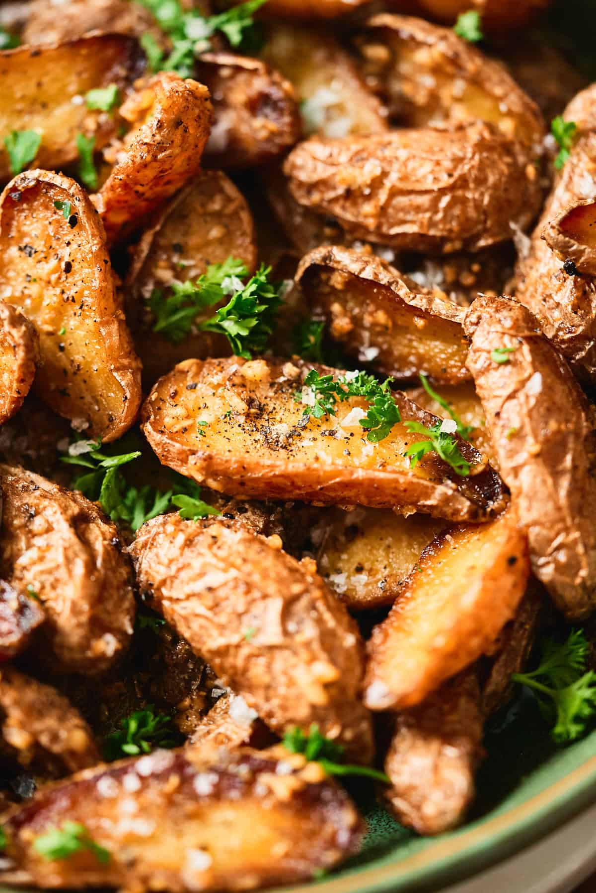 Macro shot of crispy garlic butter roasted baby potatoes showing golden caramelized cut sides, parsley, and flaky salt.