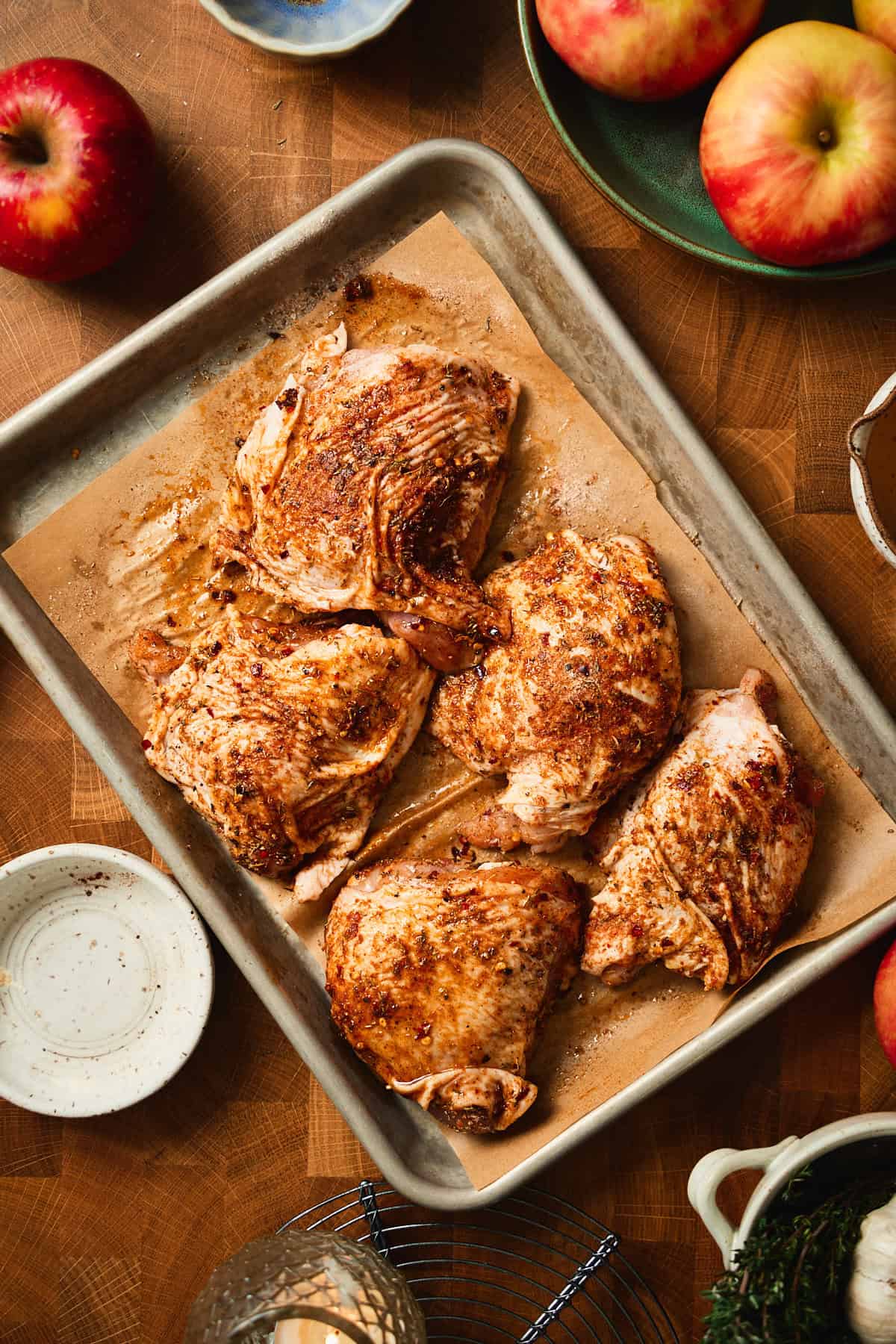Well-oiled and seasoned raw chicken thighs on a parchment-lined sheet pan, ready to sear.
