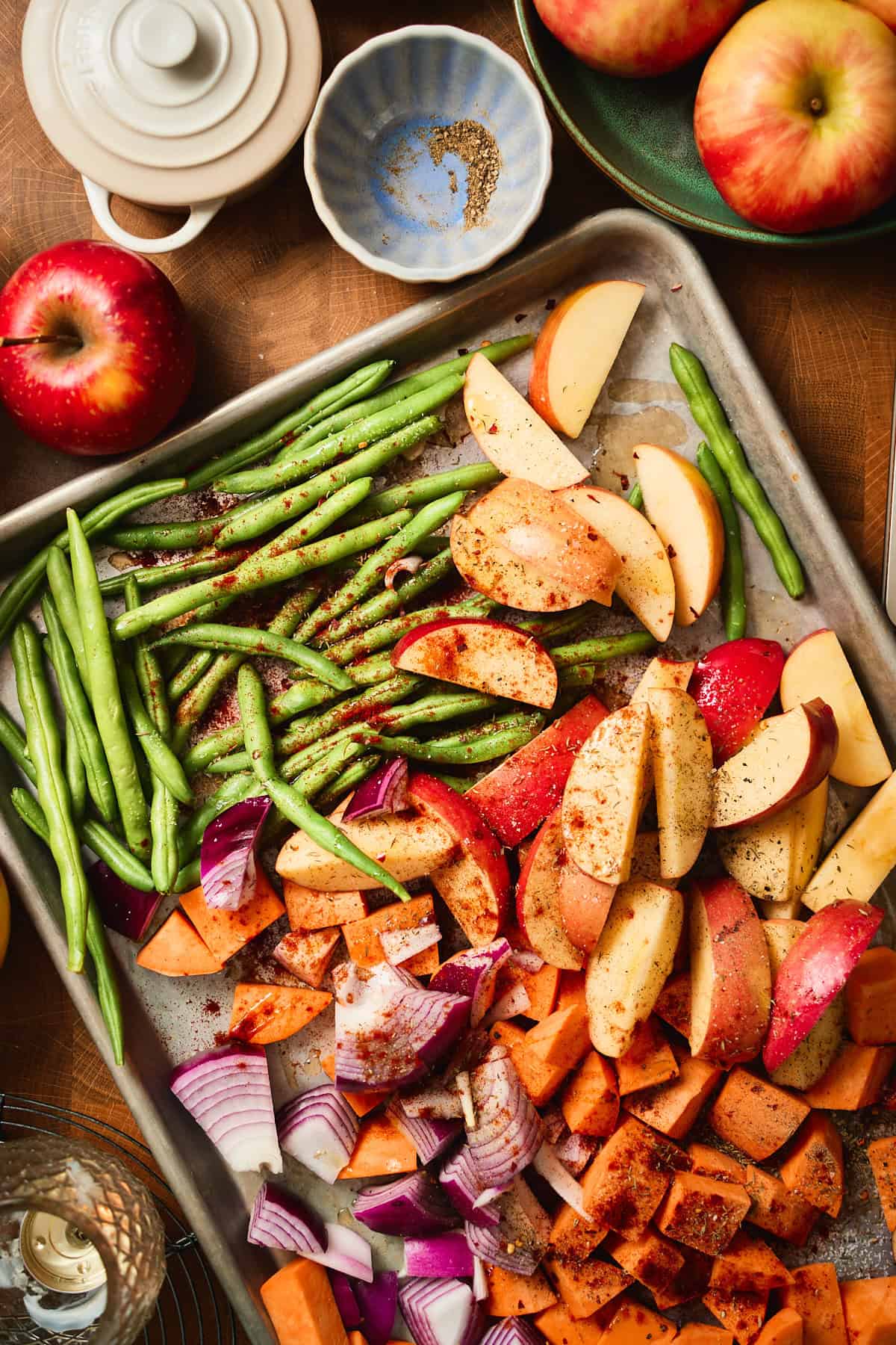 Seasoned apple wedges, sweet potatoes, green beans, and red onion spread on a sheet pan before roasting.