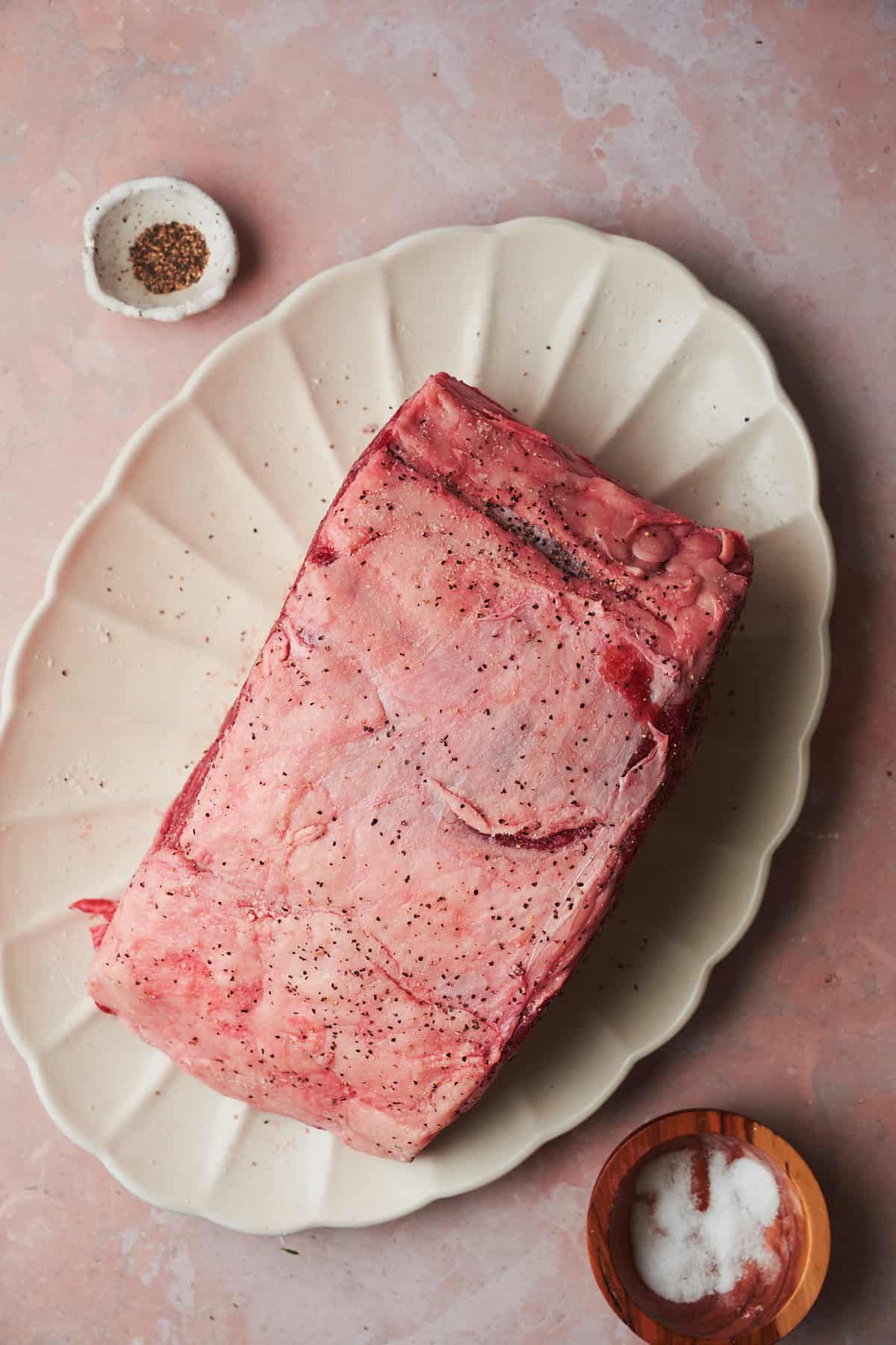 prime rib seasoned with salt and pepper on a white ruffled plate.