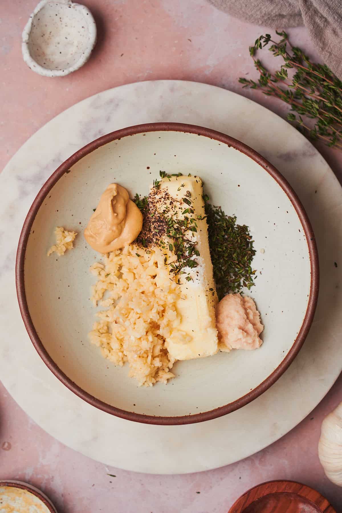 stick of butter in a bowl with thyme, salt, dijon mustard, pepper, and minced garlic.