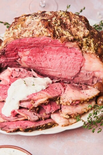 Slow Cooker Prime Rib on a platter with thyme, roasted baby potatoes, and horseradish sauce.