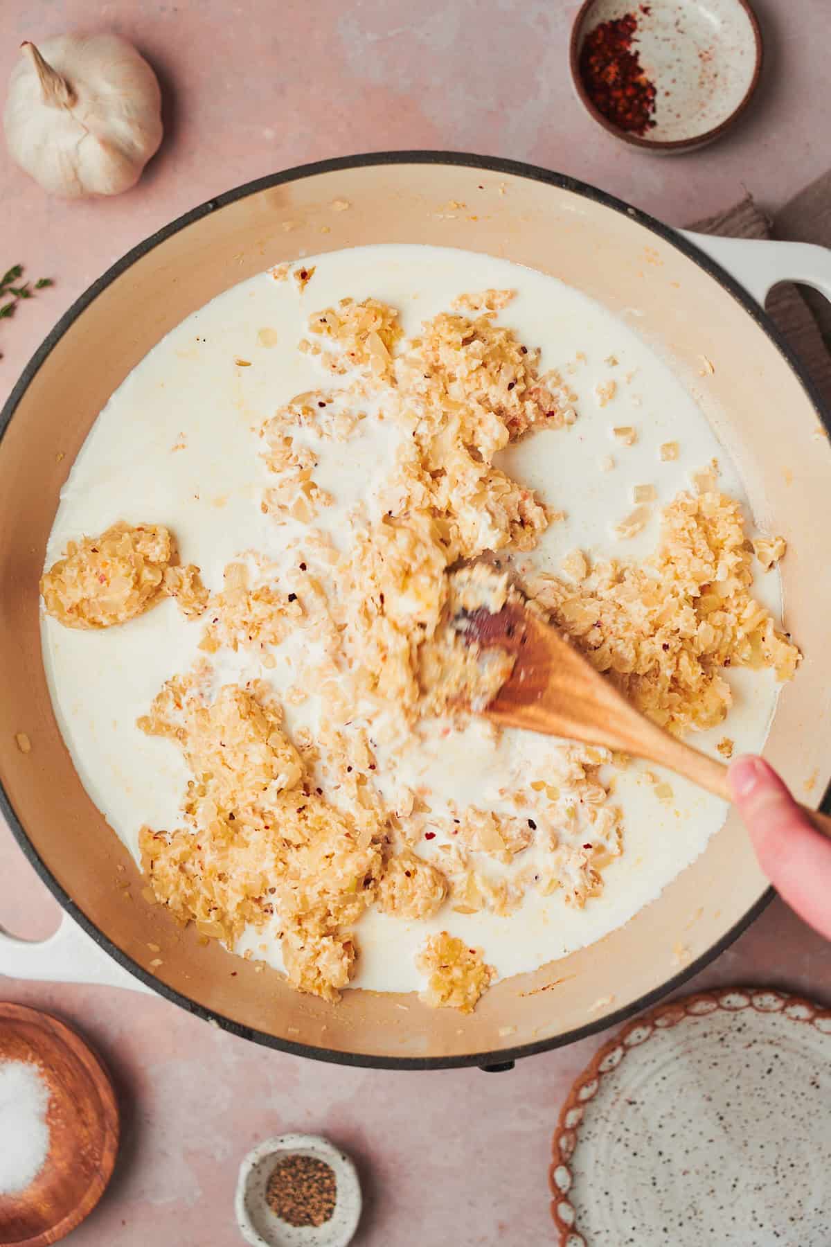 half and half in a skillet with a wooden spoon and onions and cream cheese mixed into it.