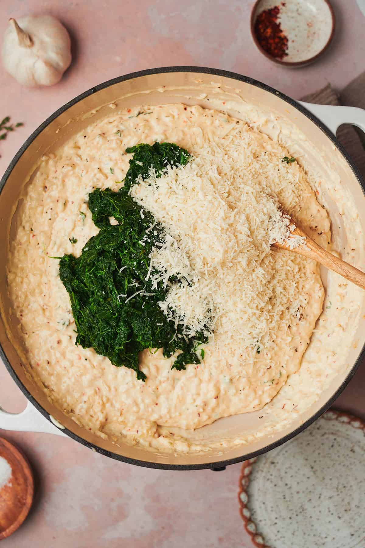 spinach and some parmesan cheese added to a skillet with a creamy sauce in it.