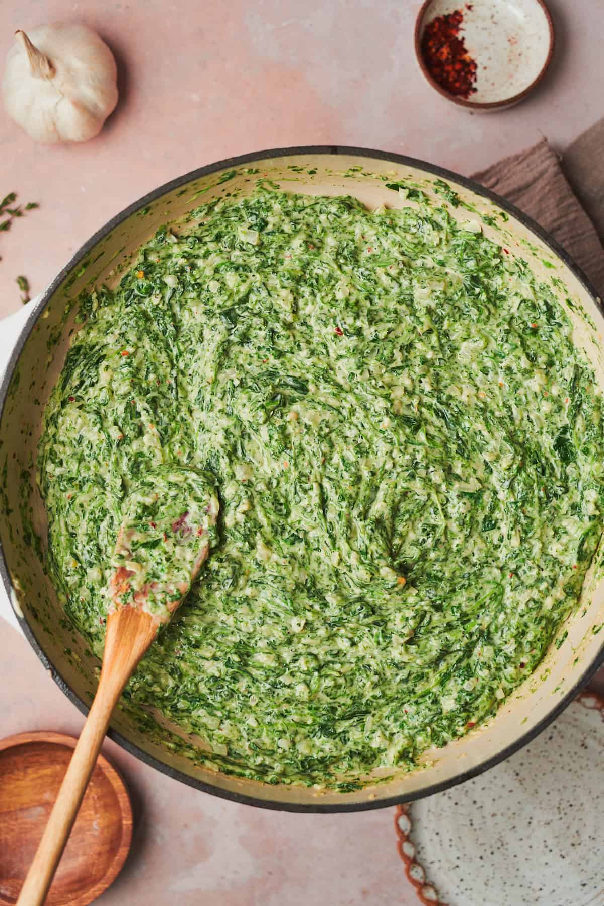 bright green creamed spinach in a skillet with a wooden spoon.