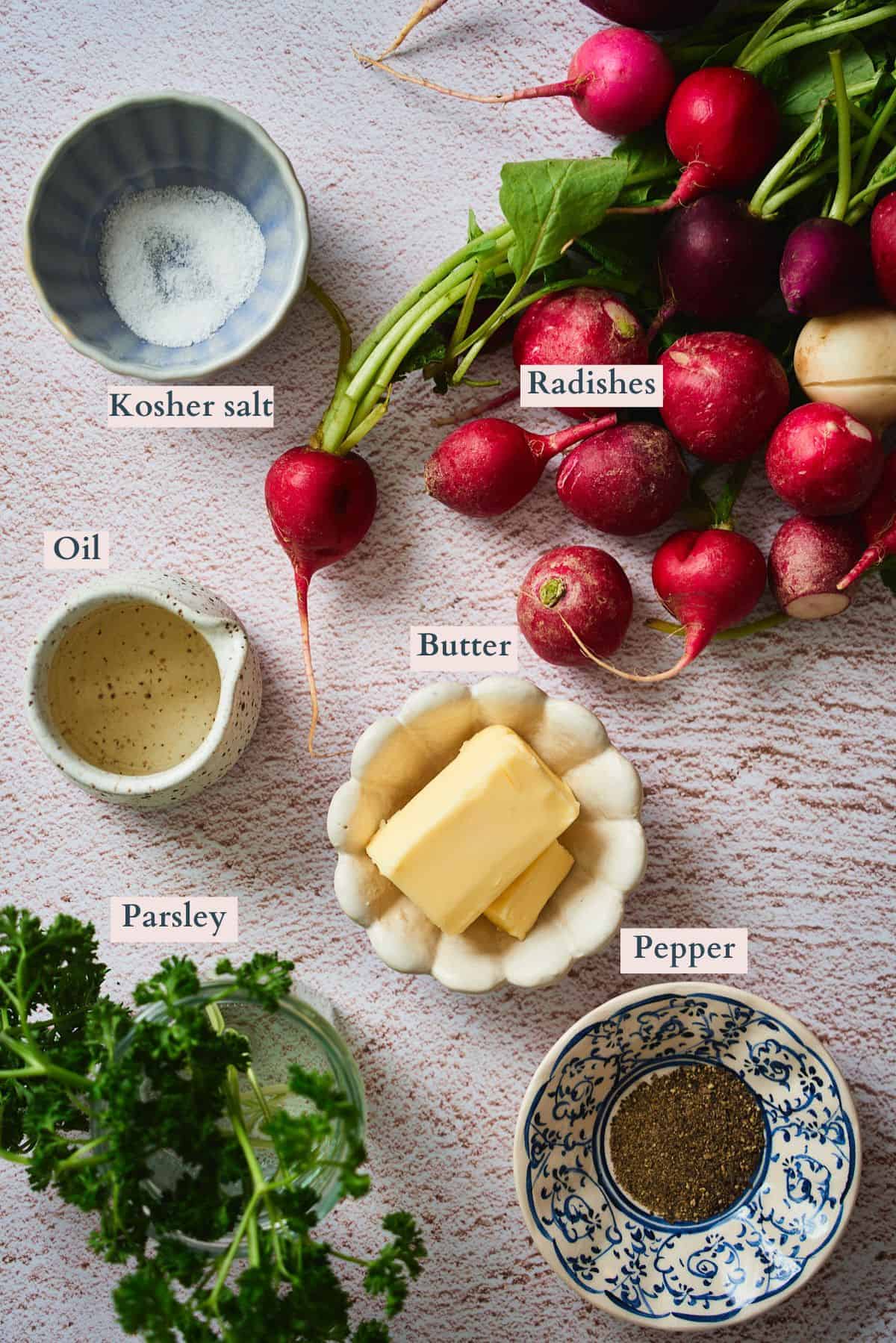 Ingredients for roasted radishes with brown butter labeled on a flat lay: radishes, butter, oil, kosher salt, parsley, and pepper.
