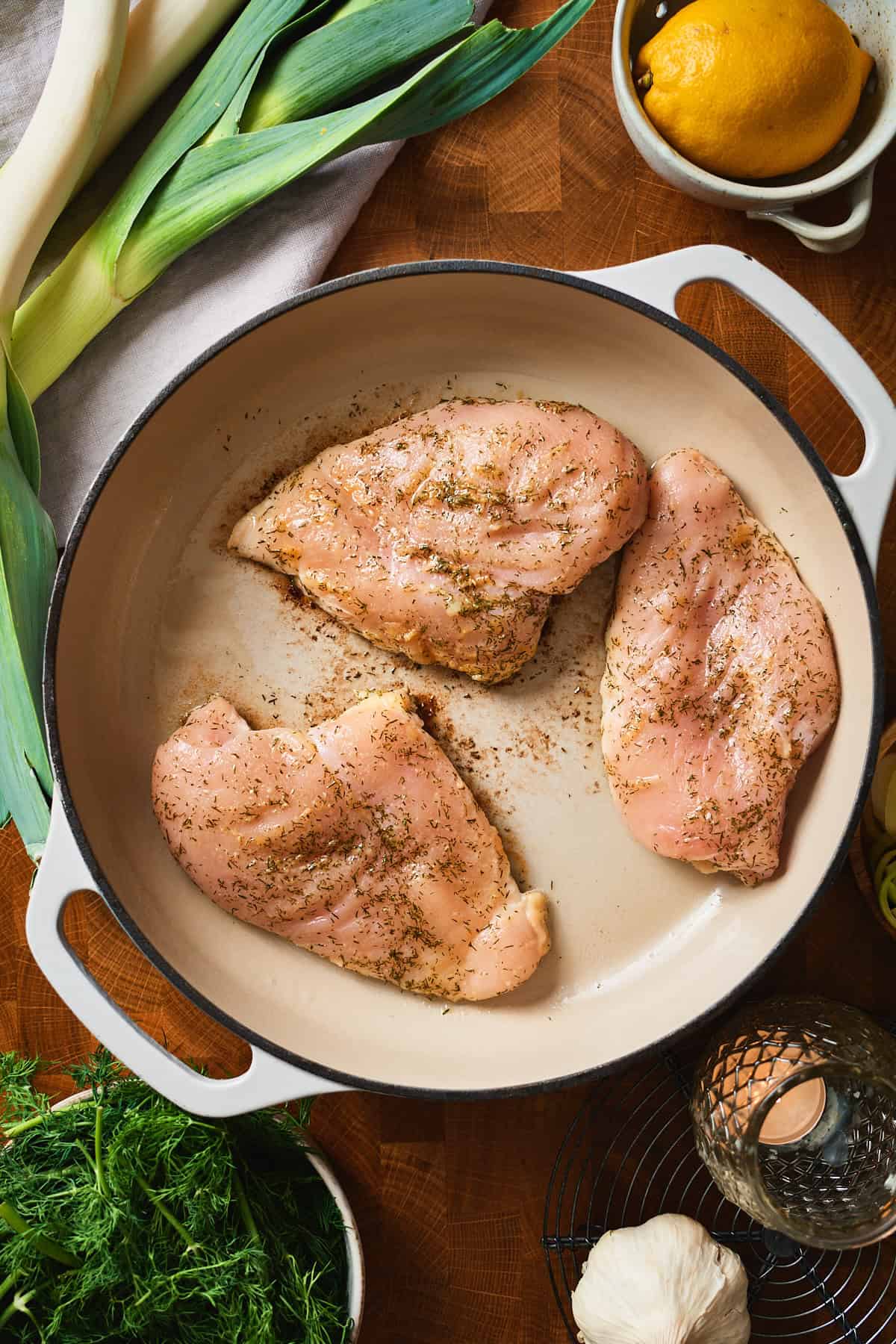 Three seasoned raw chicken breasts in a white enameled pan.