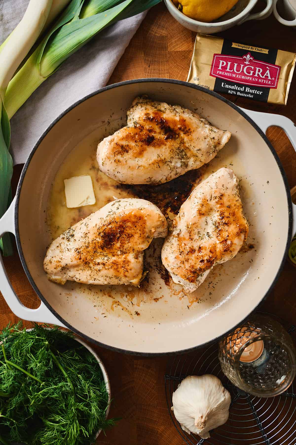 Seared chicken breasts in a pan with a pat of butter melting alongside.