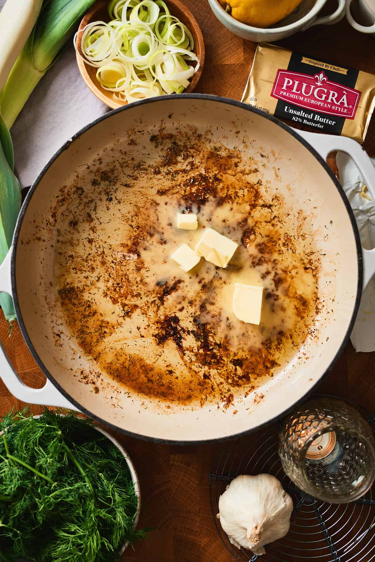 Overhead view of a white pan with golden fond and butter pats beginning to melt.
