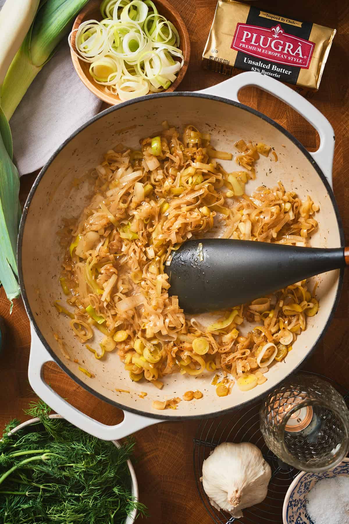 Golden caramelized leeks in a white enameled pan.